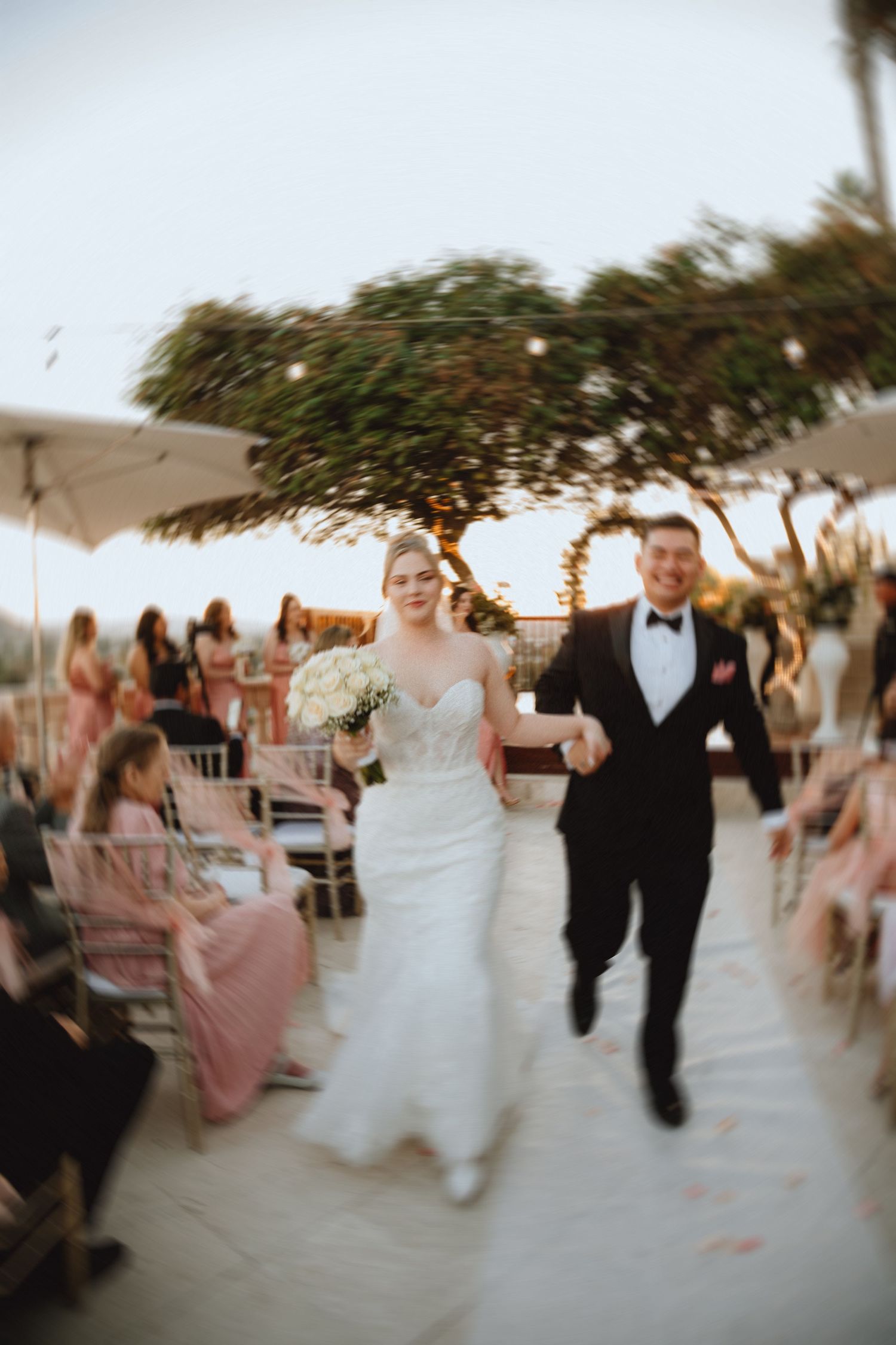 Newlyweds exit their ceremony through guests on an outdoor terrace.