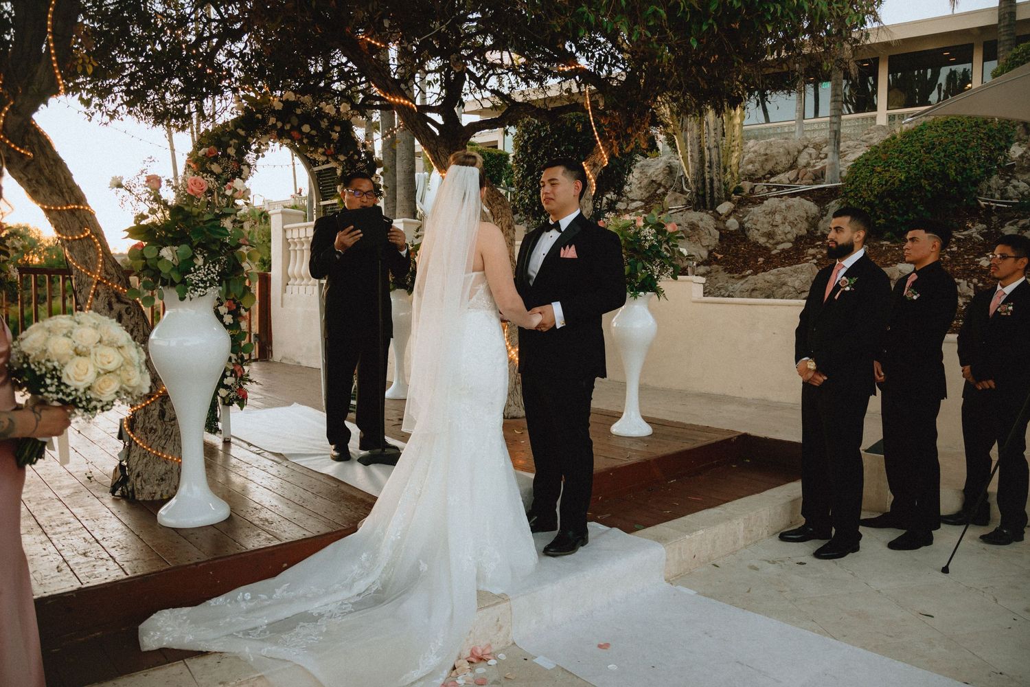 Intimate outdoor wedding ceremony with attendants standing beside a wooden platform.