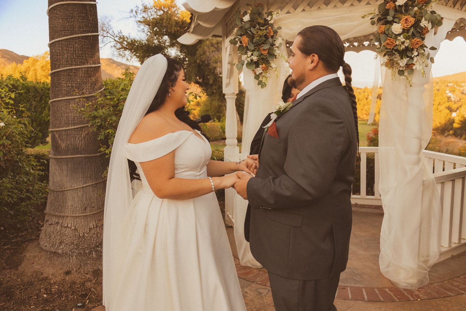 Couple exchanges vows under ornate gazebo during sunset wedding ceremony.