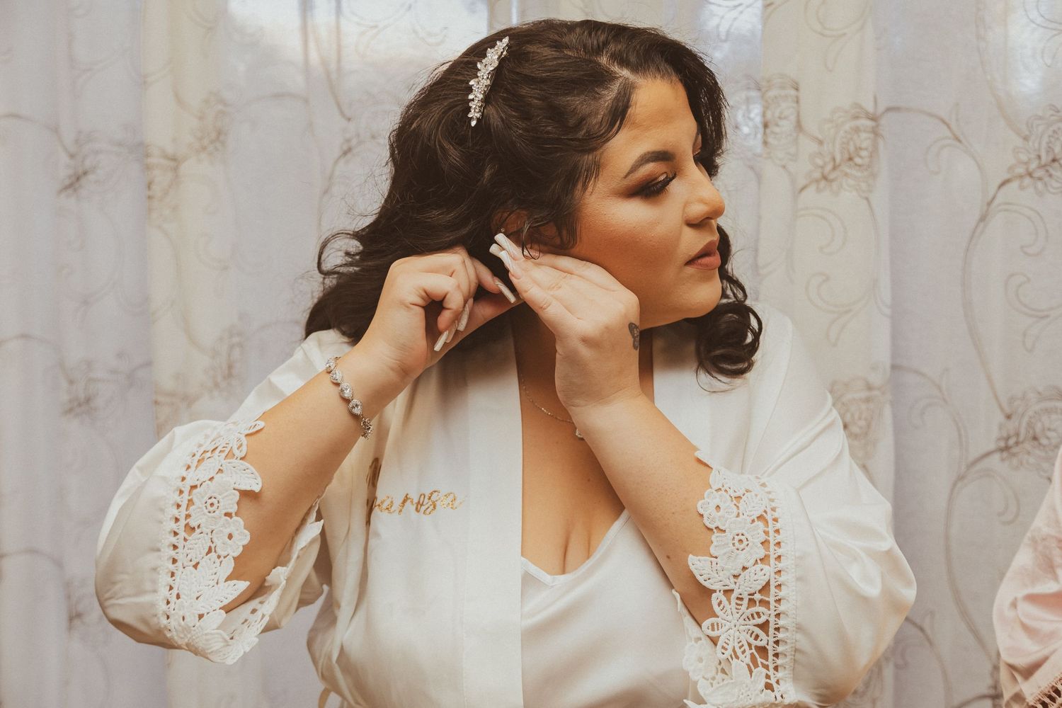 A woman in white adjusts her earrings while getting ready.
