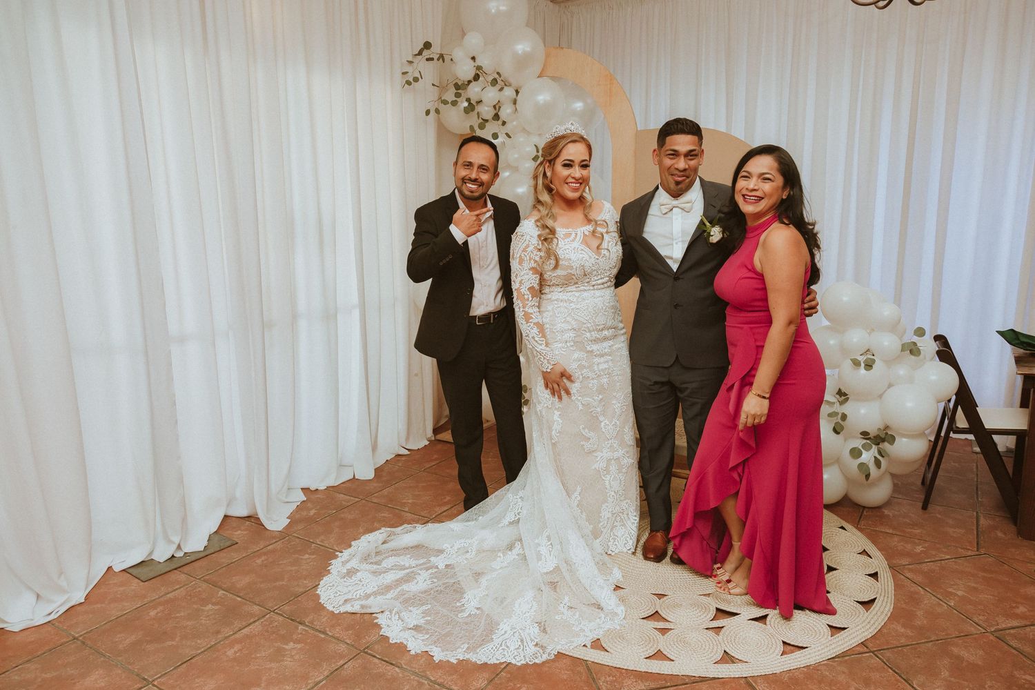 Wedding party poses in front of white balloon arch and floral backdrop.