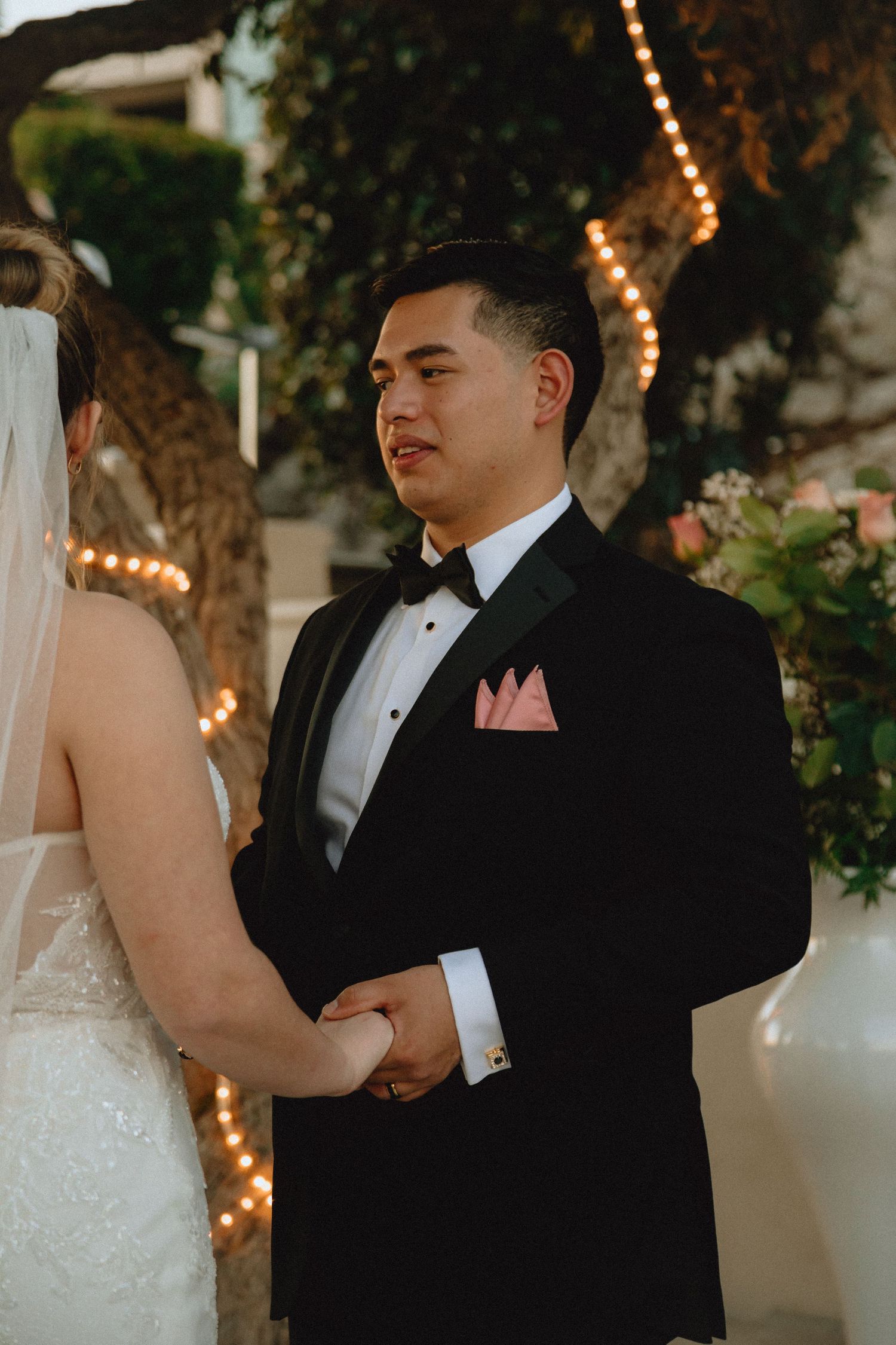 Elegant wedding ceremony with couple holding hands under string-lit trees and floral decor.