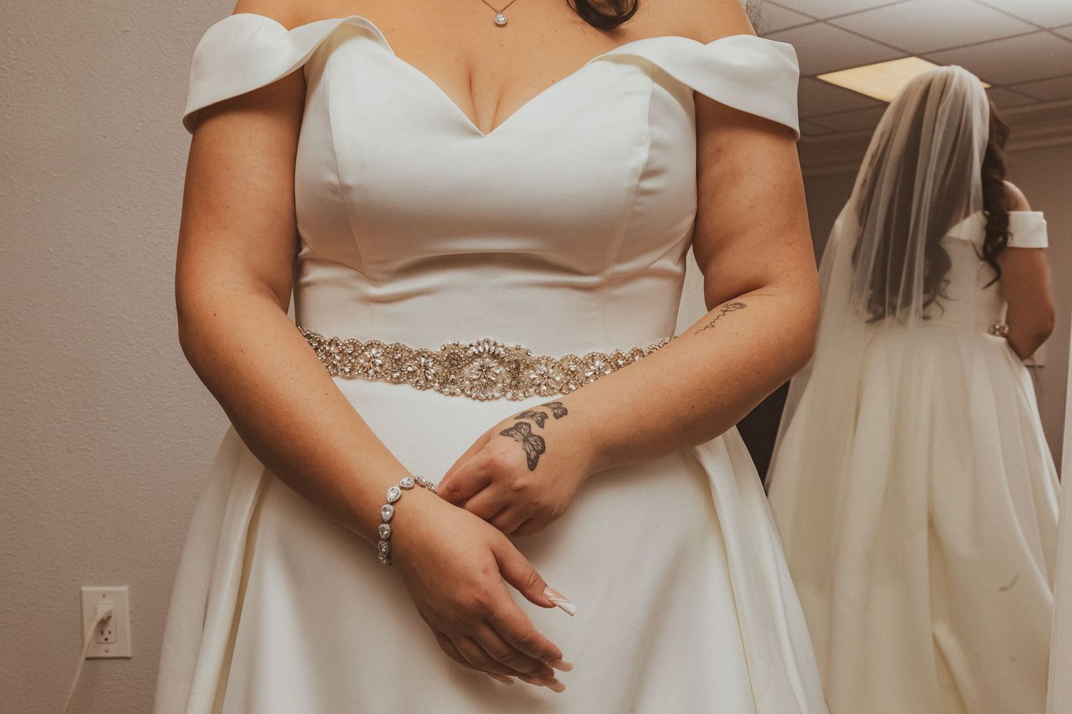 Detail shot of an elegant white wedding gown showing off-shoulder neckline and beaded belt accent.