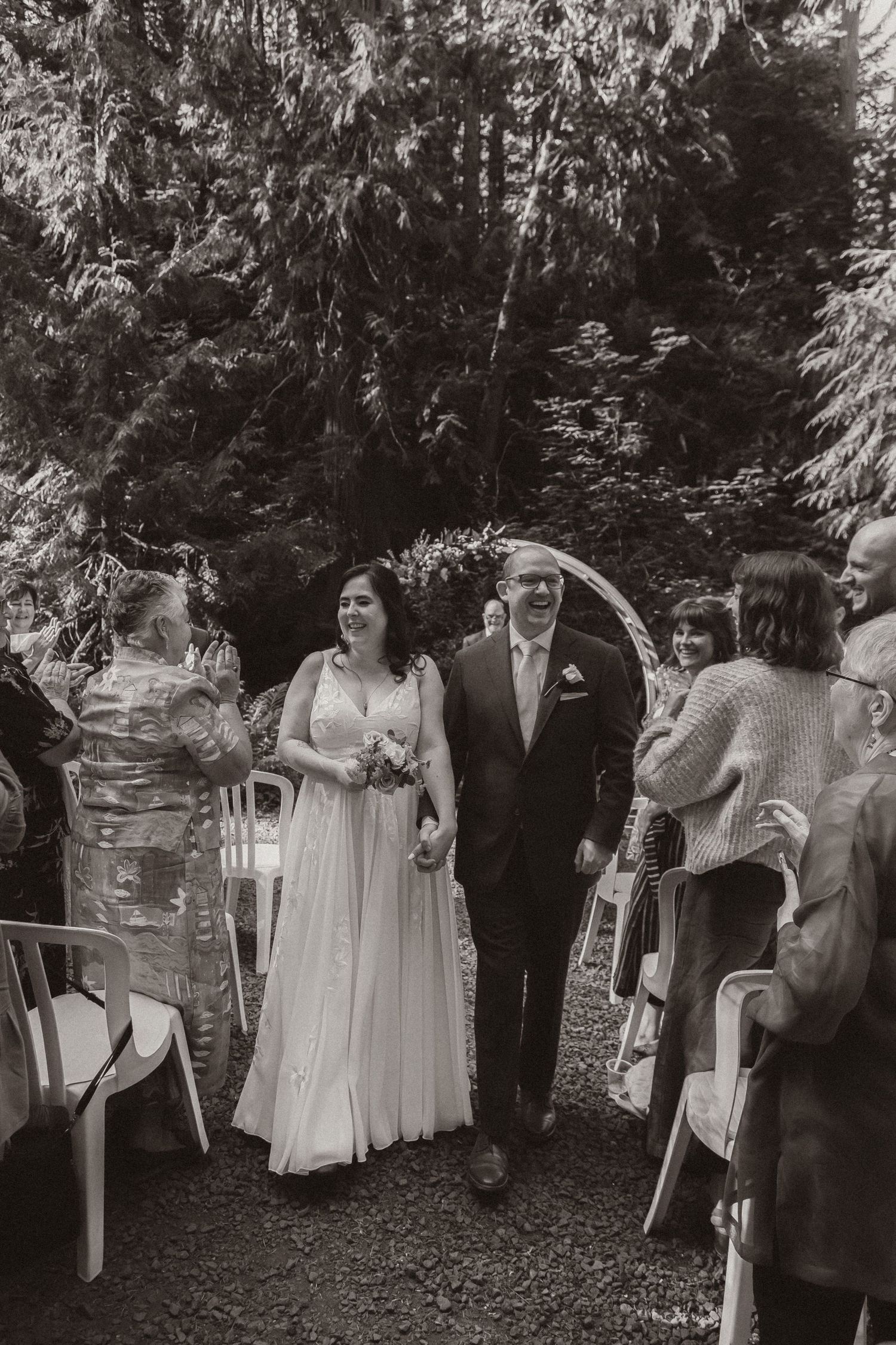 Black and white photo of wedding recessional with guests in woodland setting.