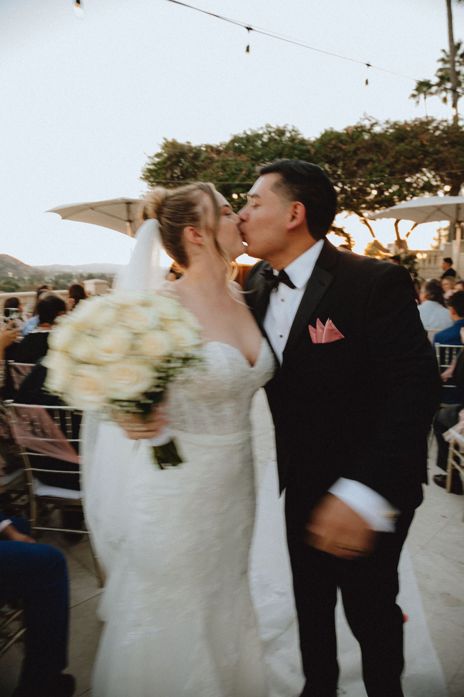 Romantic wedding kiss shared during an outdoor celebration with string lights.