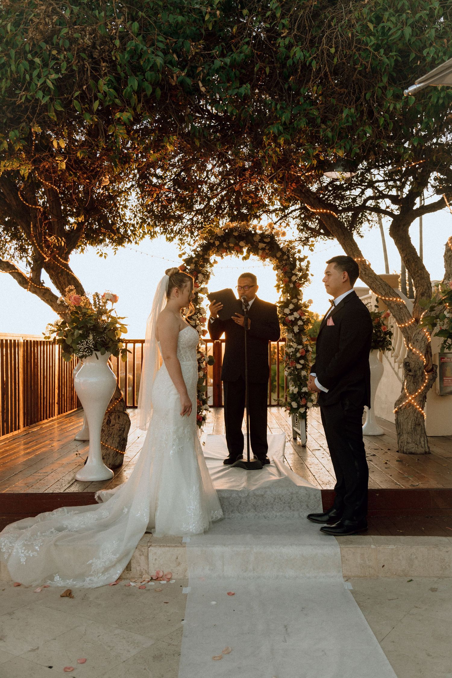 Sunset wedding ceremony on elevated deck with white pedestals holding floral arrangements.