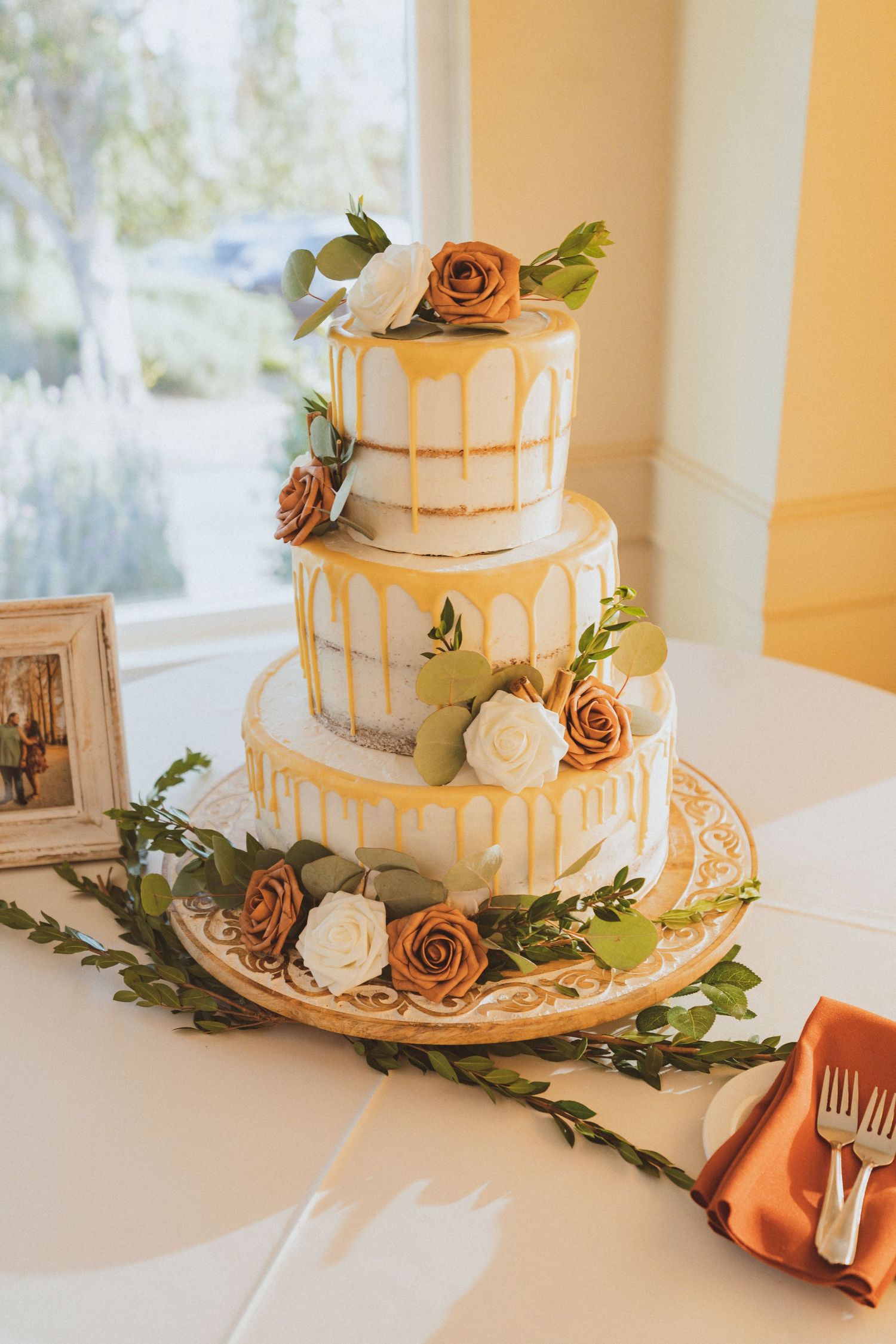 Three-tier white wedding cake with gold drip decoration and peach and cream roses.
