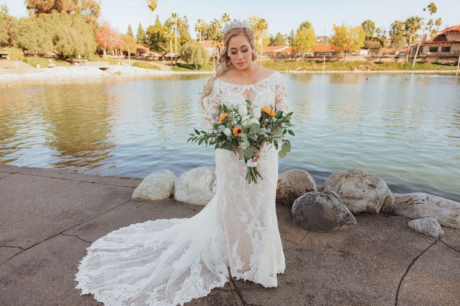 Wedding dress with long lace sleeves and flowing train captured at waterfront location.