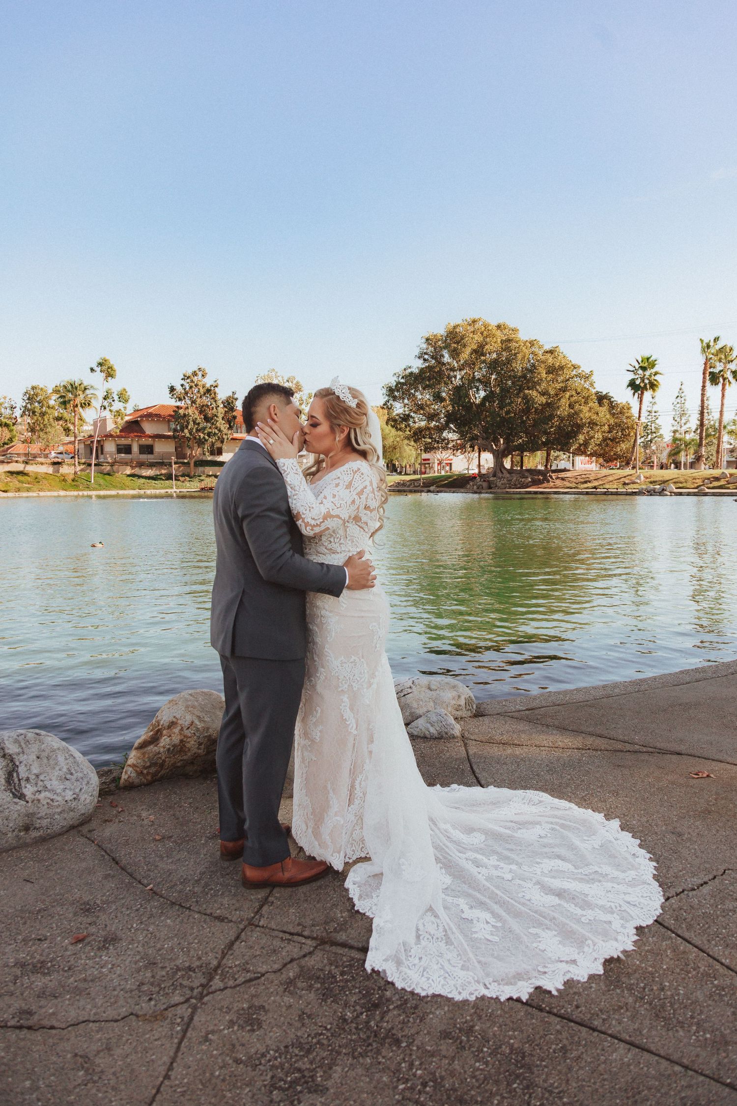 Wedding couple stands on stone pathway with beautiful lake and palm trees in background.