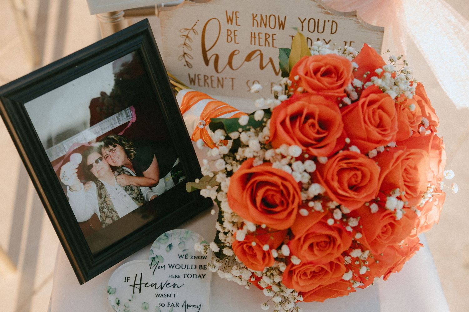 Orange rose bouquet with baby's breath displayed next to framed wedding photo and decorative sign.