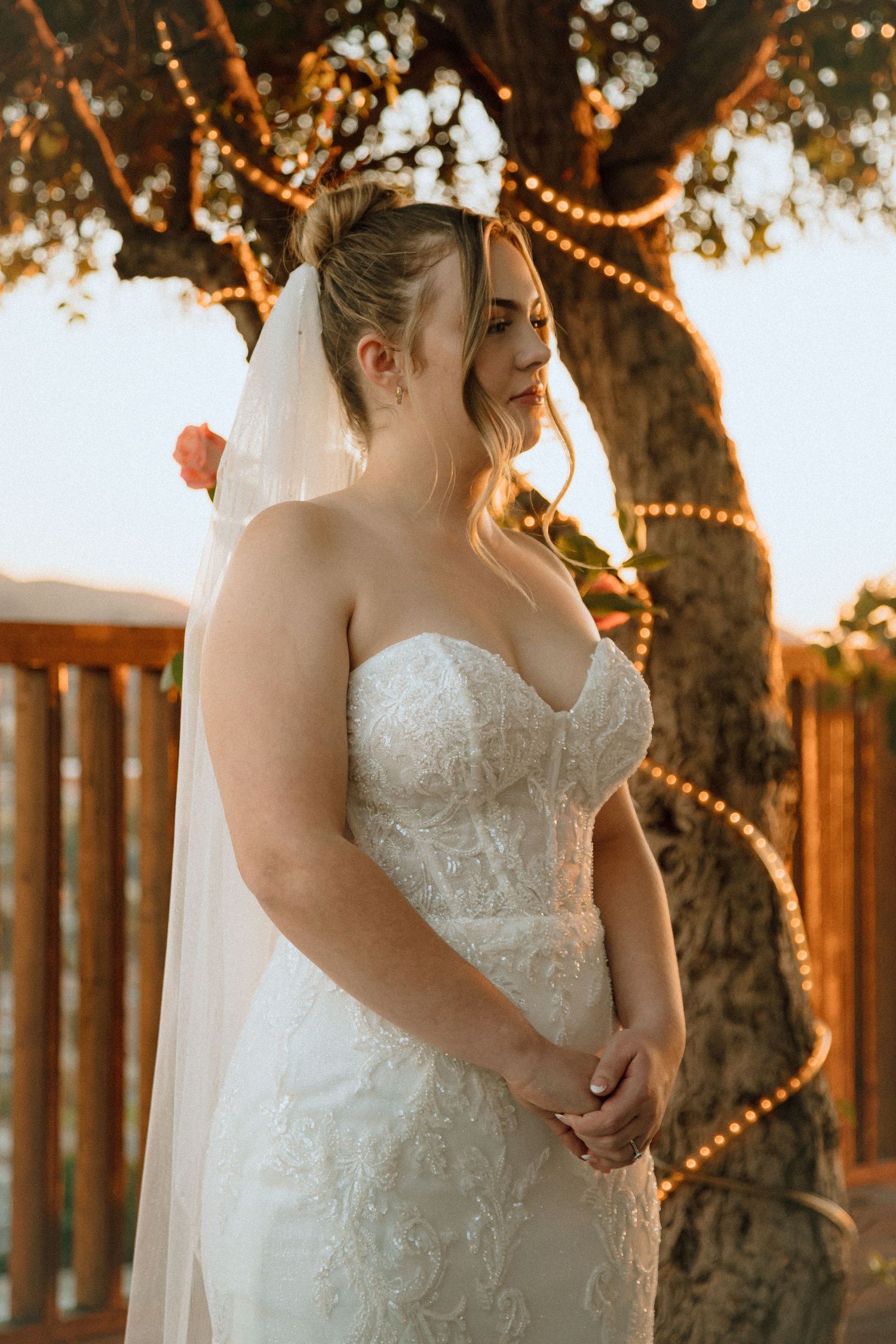 Sunset bridal portrait with twinkling lights wrapped around a tree in the background.