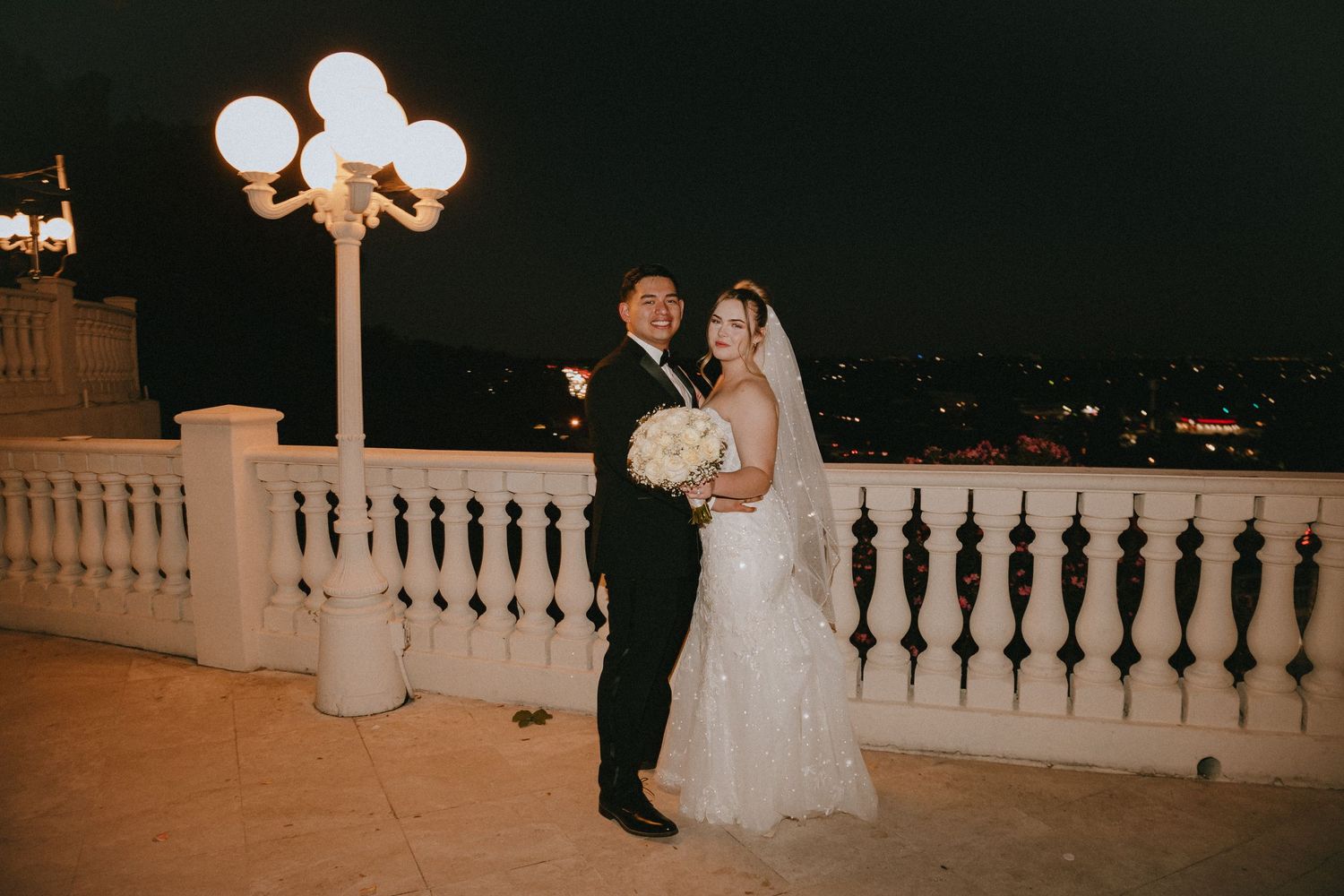 Wedding portrait at night with decorative railing and glowing vintage lamp post.