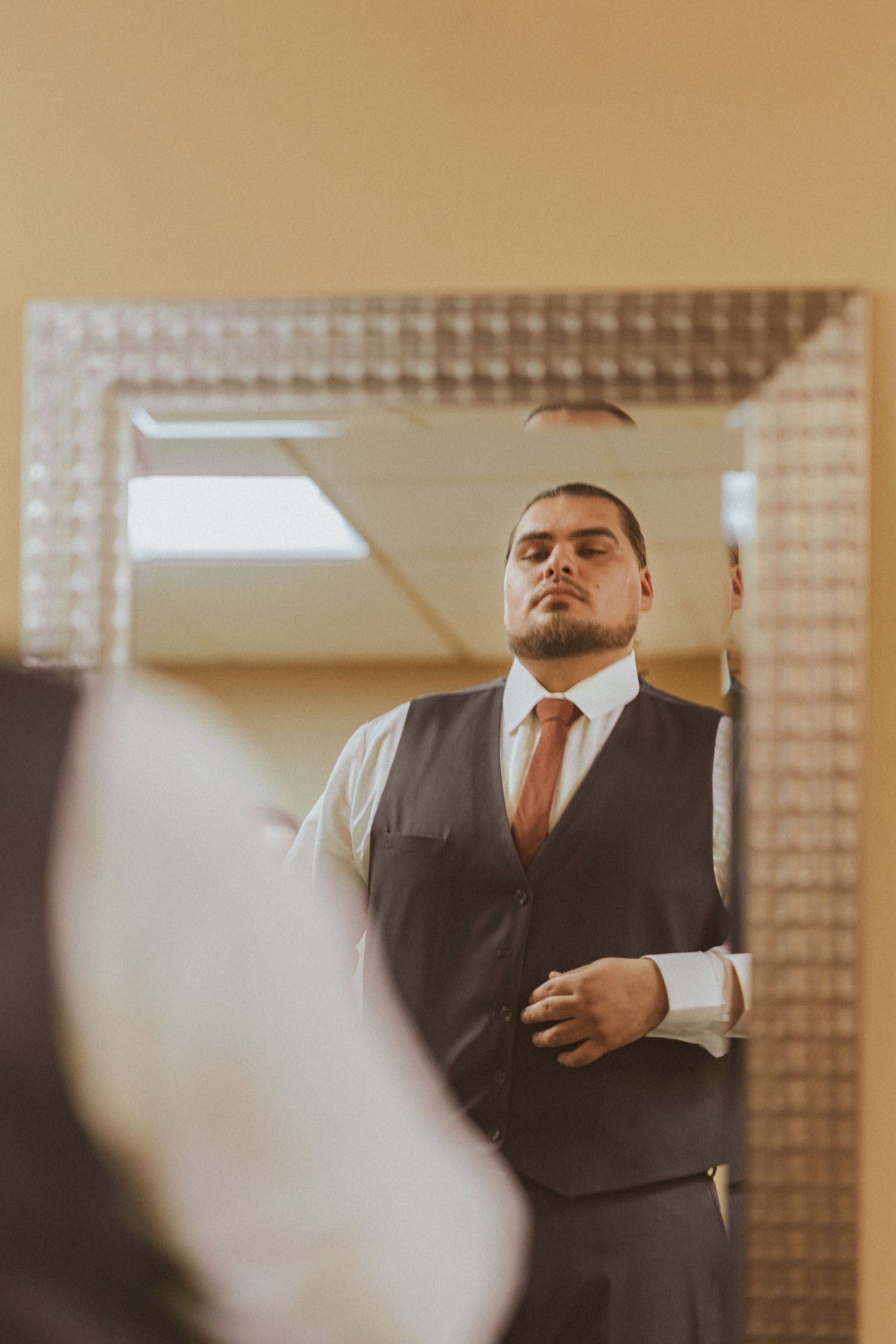 Person in formal vest and tie looks confidently in mirror while getting ready.