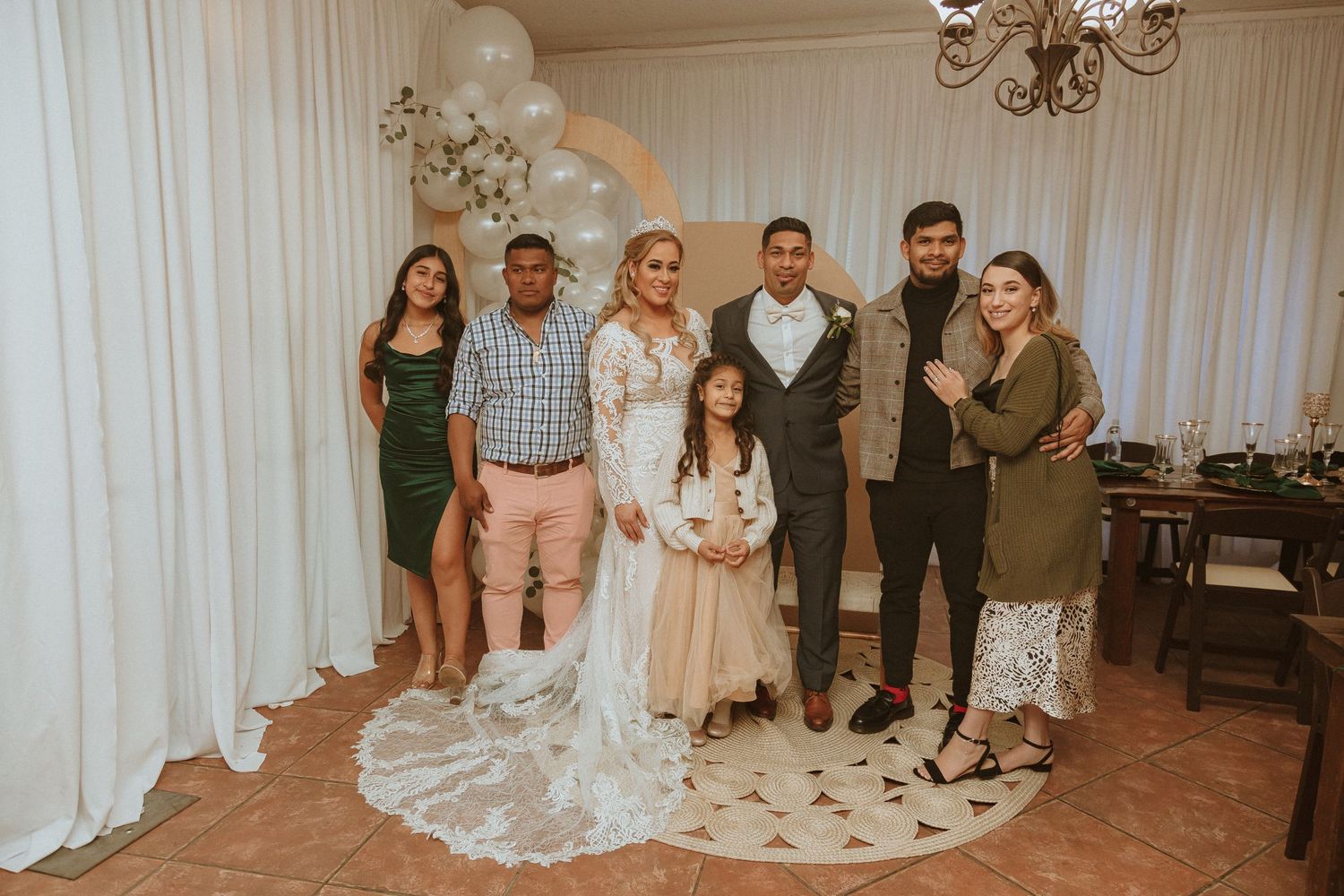 Wedding party poses together against white backdrop with crescent moon decoration and white balloons.