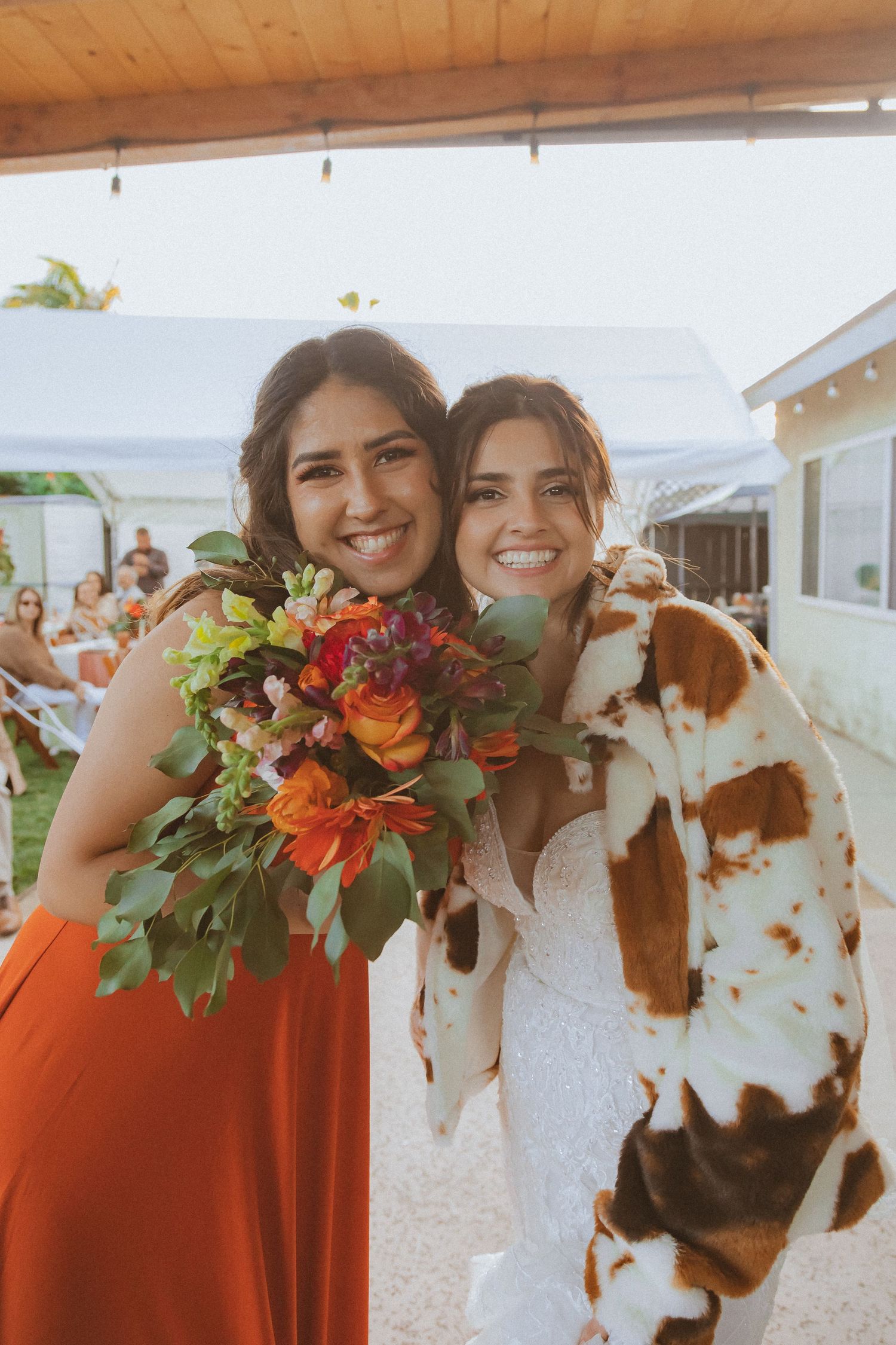 Two wedding attendants share a joyful moment with bright orange floral bouquets.