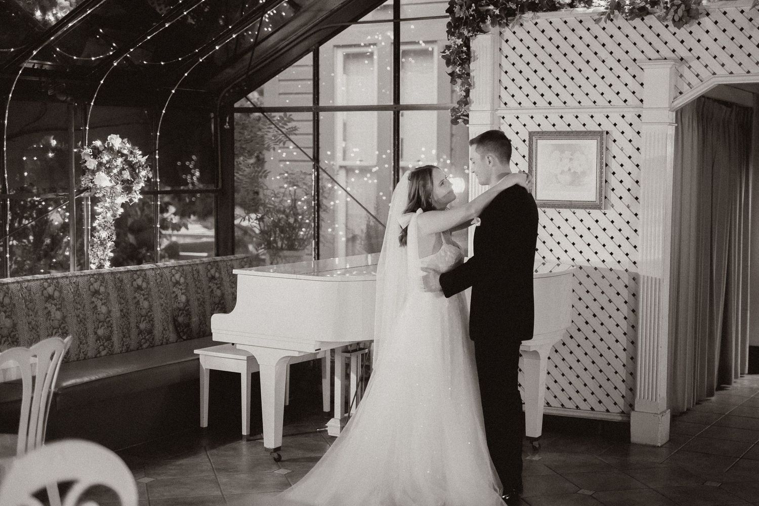 Vintage-style wedding photo of couple's dance near grand piano and decorative lattice wall.