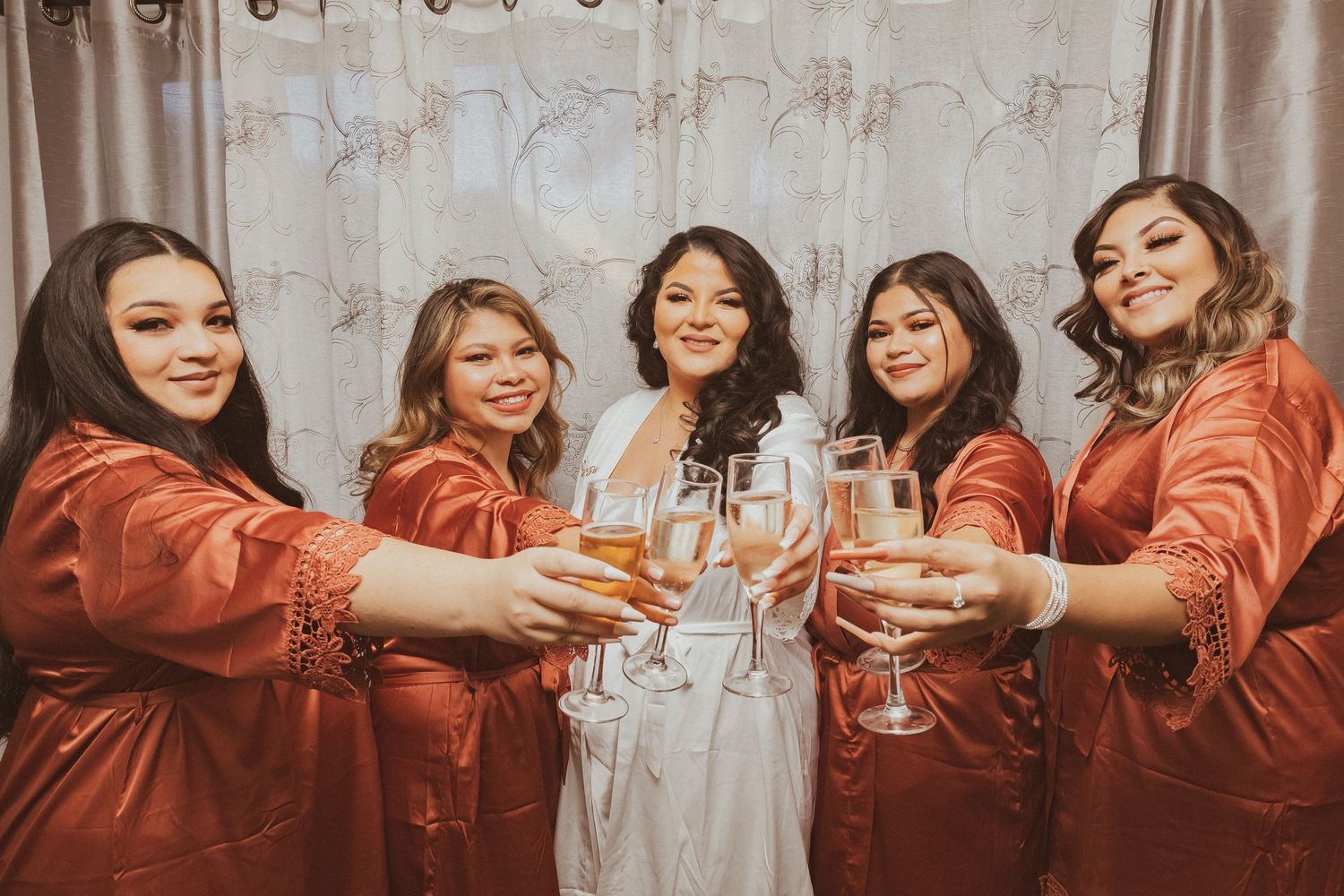 Wedding party in silk robes raises glasses together in a celebratory toast.