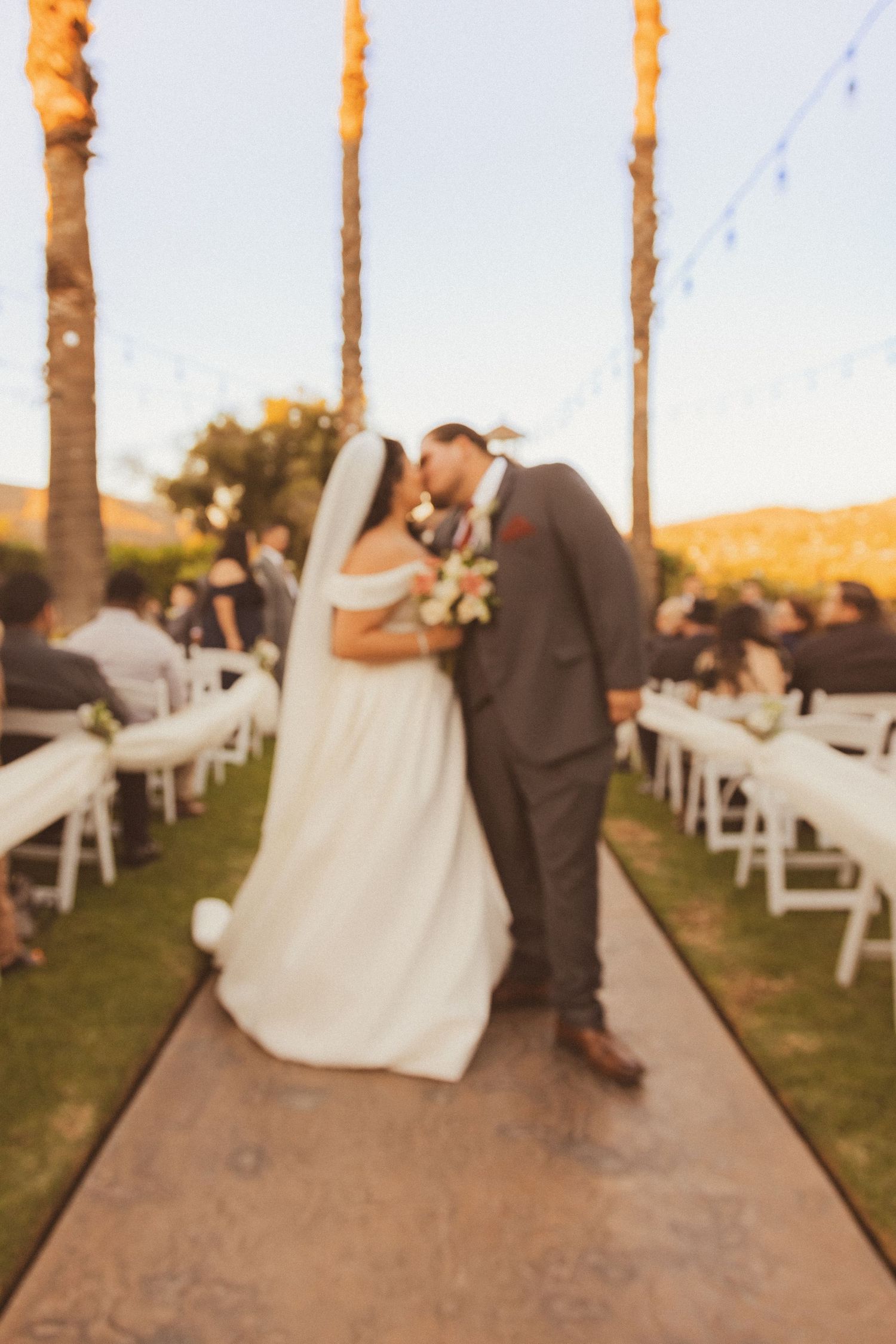 Newlyweds share a romantic moment on their wedding aisle with string lights and palm trees overhead.