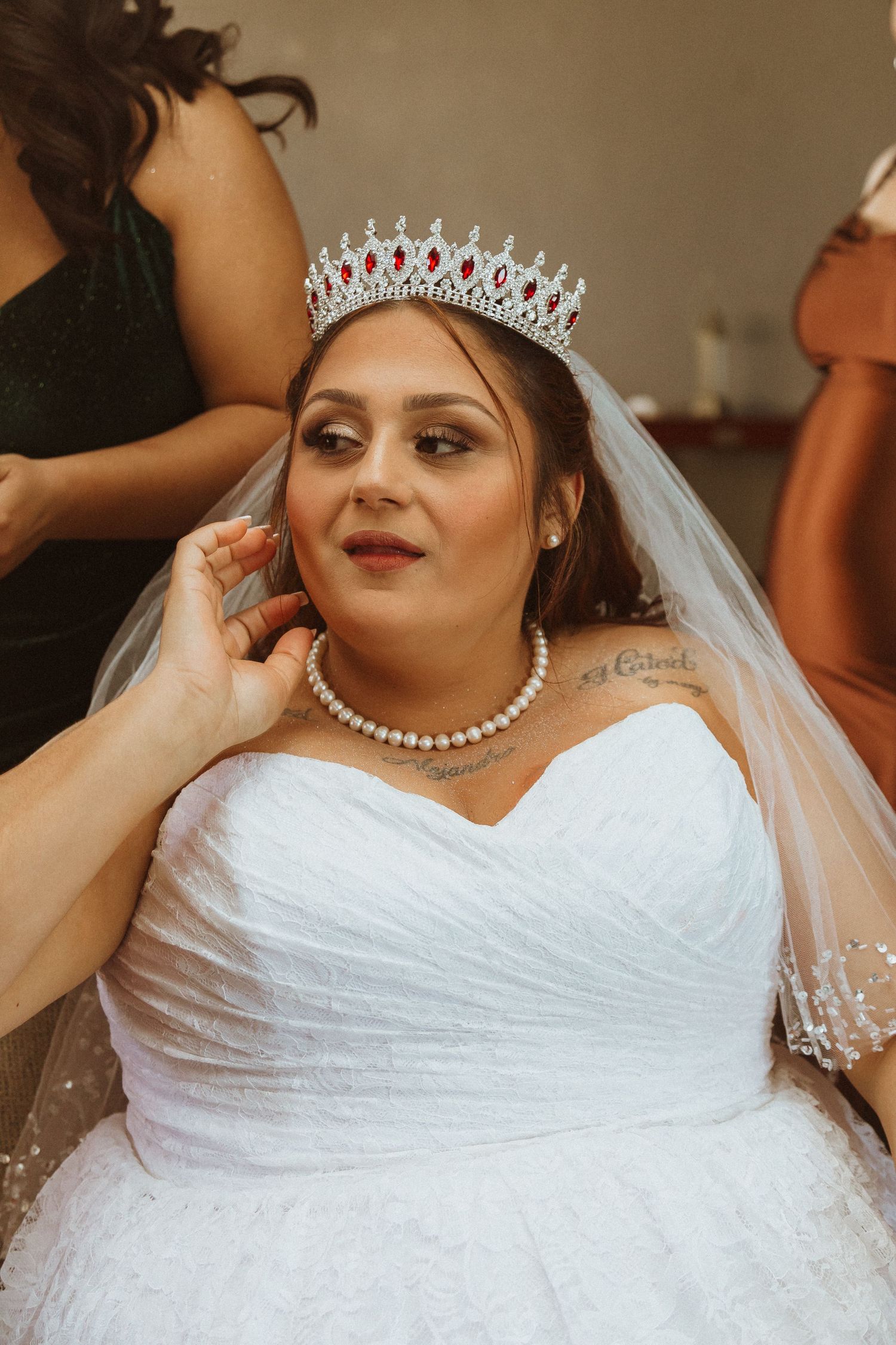 A bride in a white dress wears an elegant tiara and pearl necklace on her wedding day.