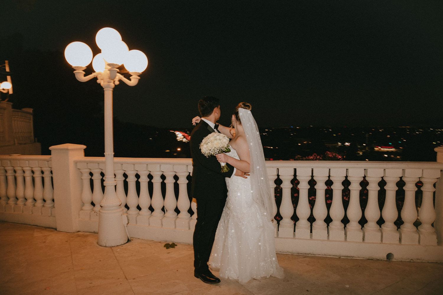 Candid wedding moment captured on elegant balcony with illuminated street lamp.