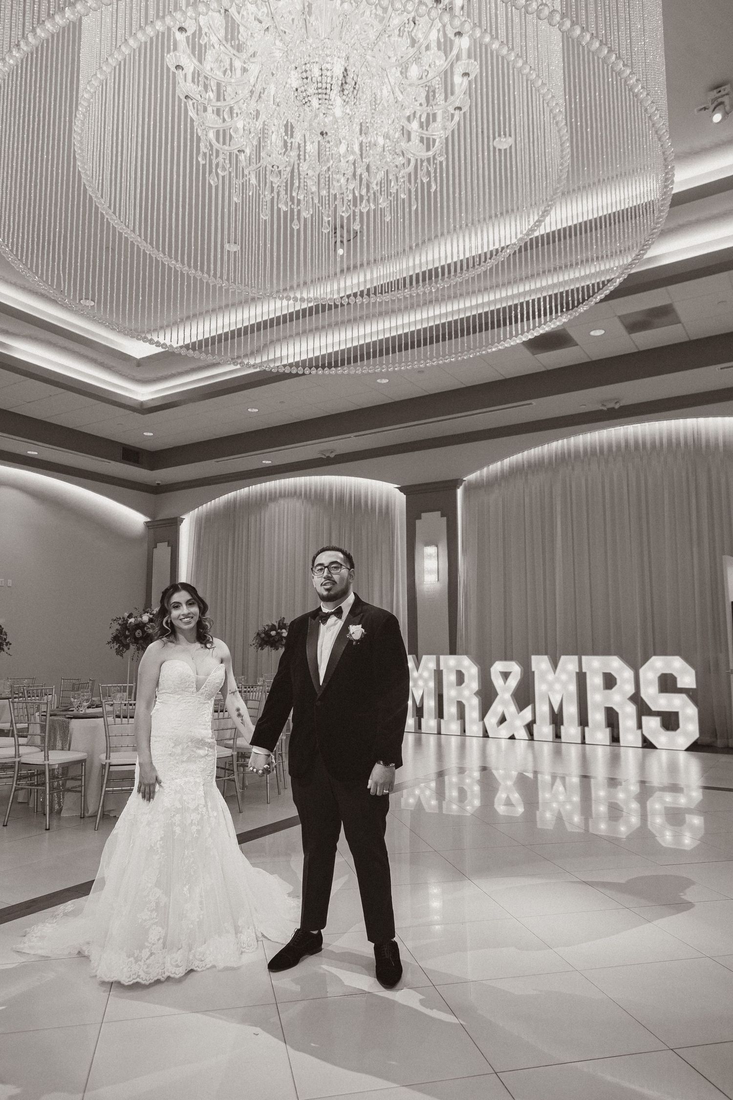 Elegant wedding ballroom with illuminated MR&MRS sign and crystal chandelier featuring a romantic black and white scene.