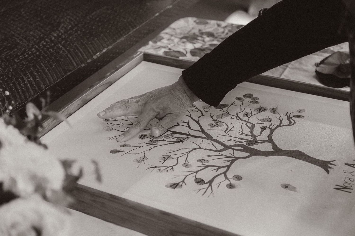 Close-up of hands signing a decorative tree illustration in a guestbook.