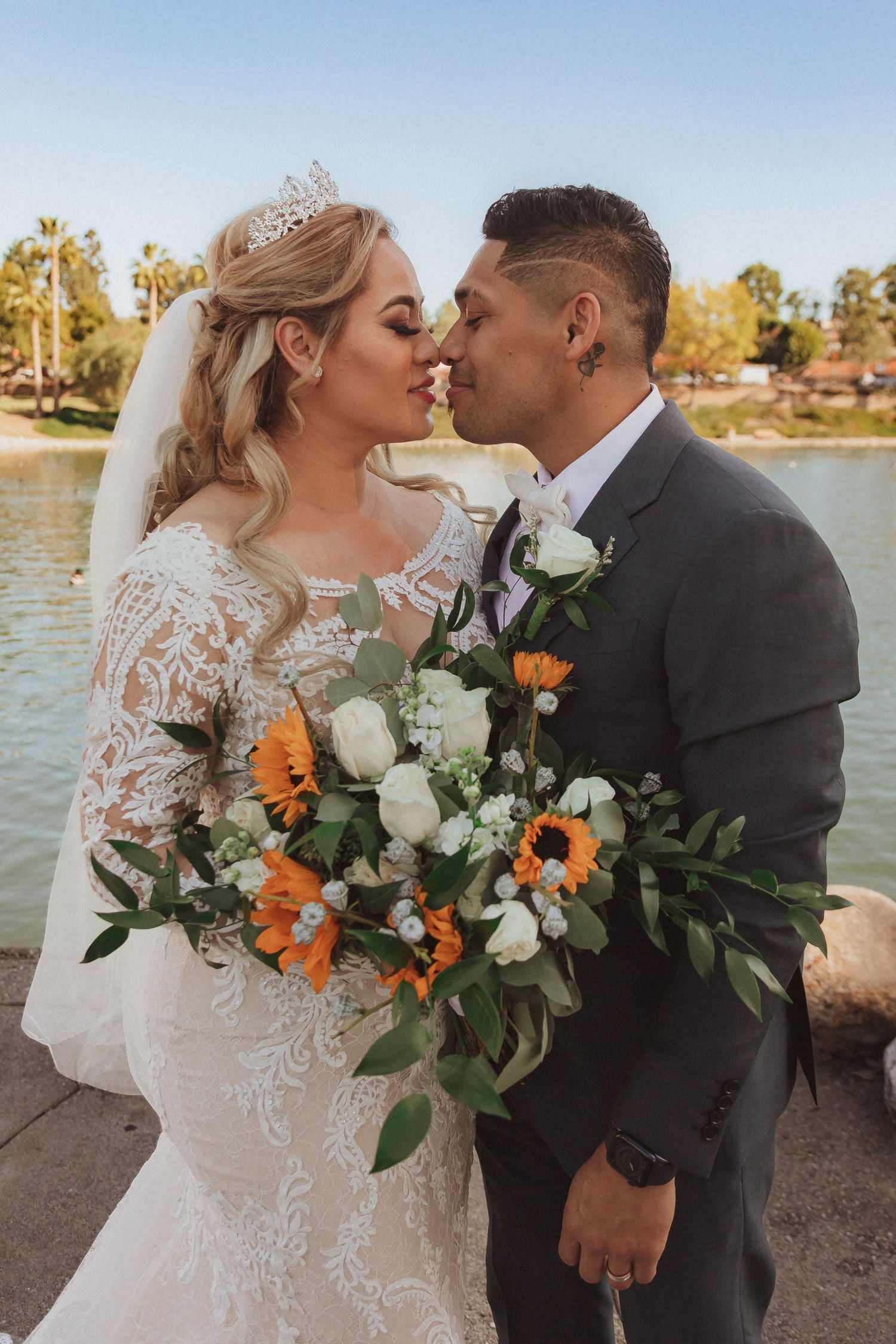Intimate lakeside wedding moment with stunning floral bouquet featuring sunflowers and roses.