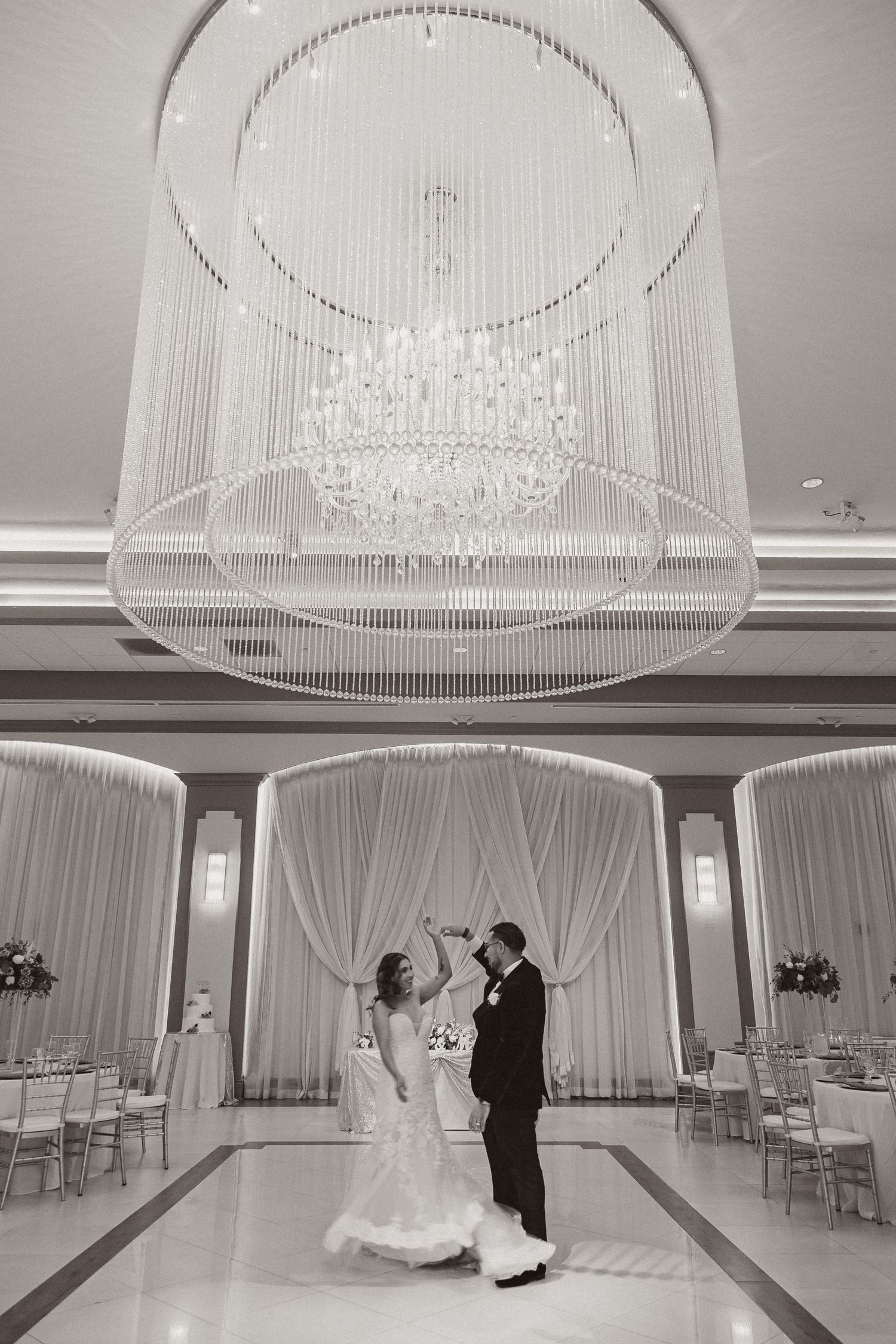 A celebratory dance moment captured under a stunning crystal chandelier in an elegant reception venue.