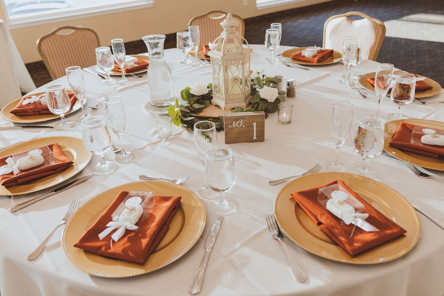 Wedding reception table setup with elegant place settings, glassware and floral centerpiece.