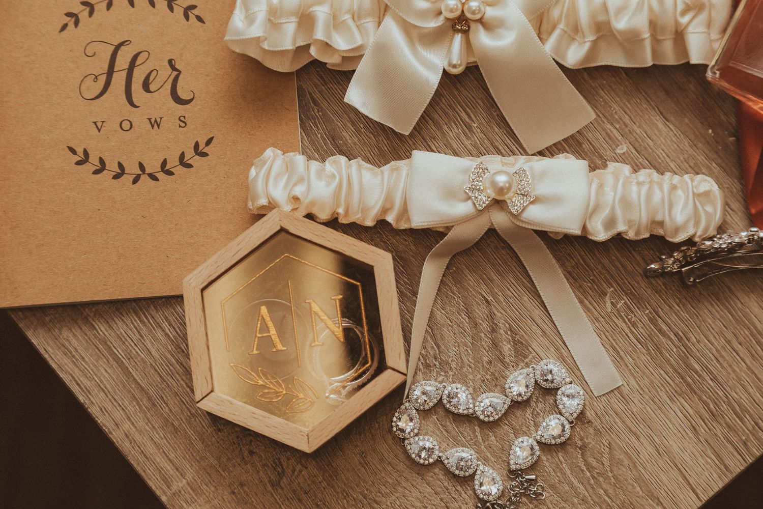 Wedding accessories including white garters, hexagonal box and pearl jewelry on wooden surface.