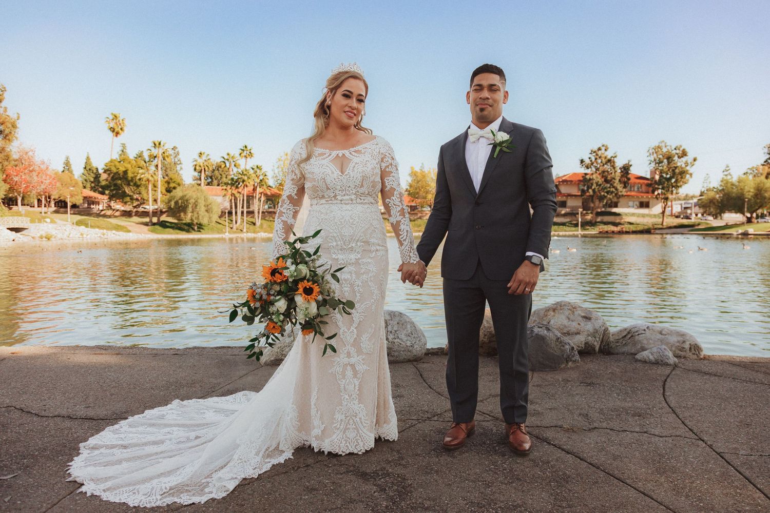 Newlyweds stand together on lakeside path during golden hour photography session.