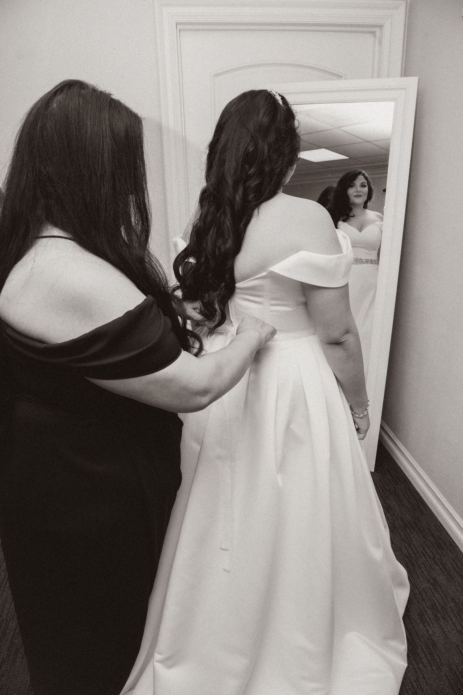 Behind-the-scenes wedding dress fitting with reflection in mirror showing final adjustments.