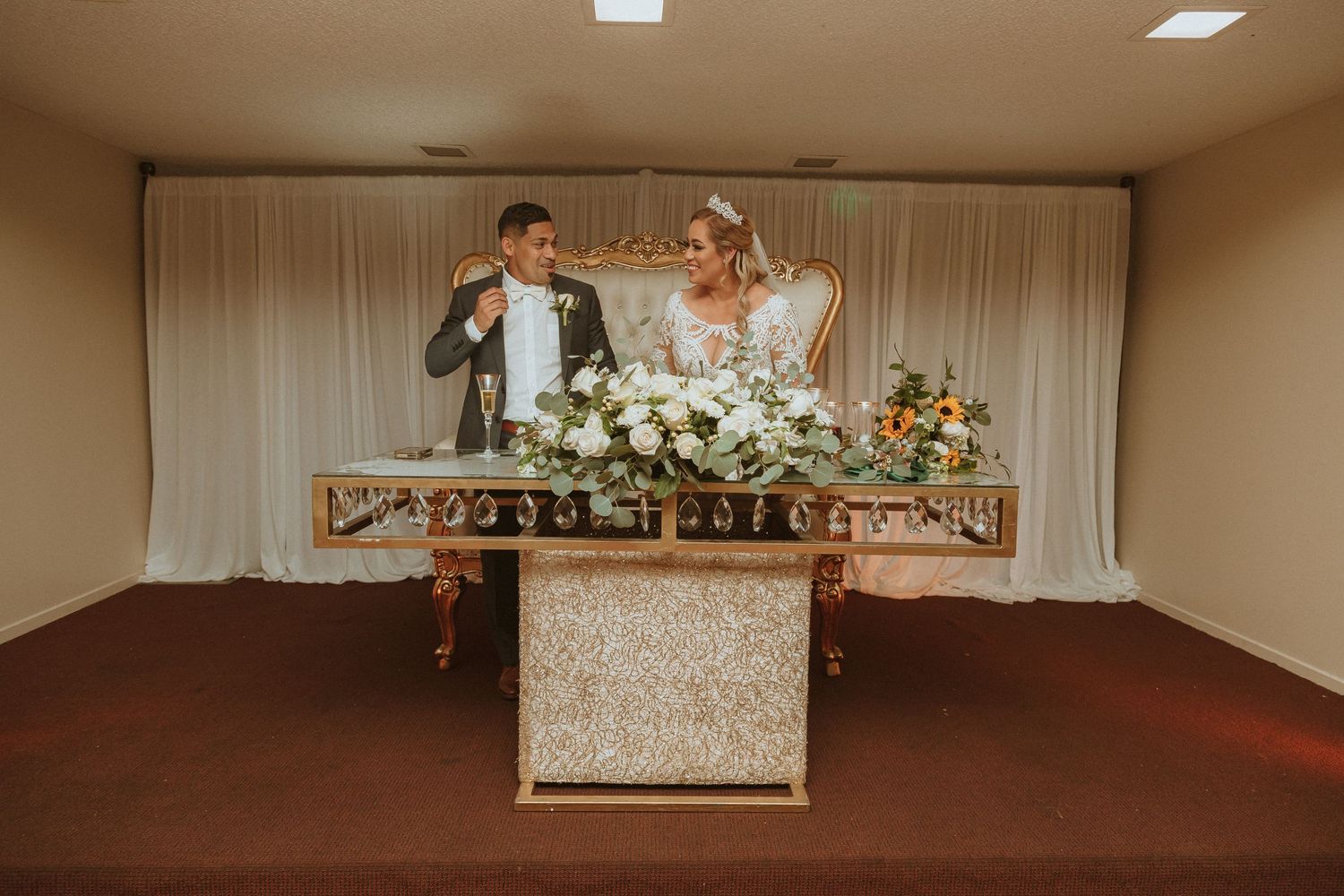 Candid shot of couple celebrating behind ornate sweetheart table with white and orange floral arrangements.