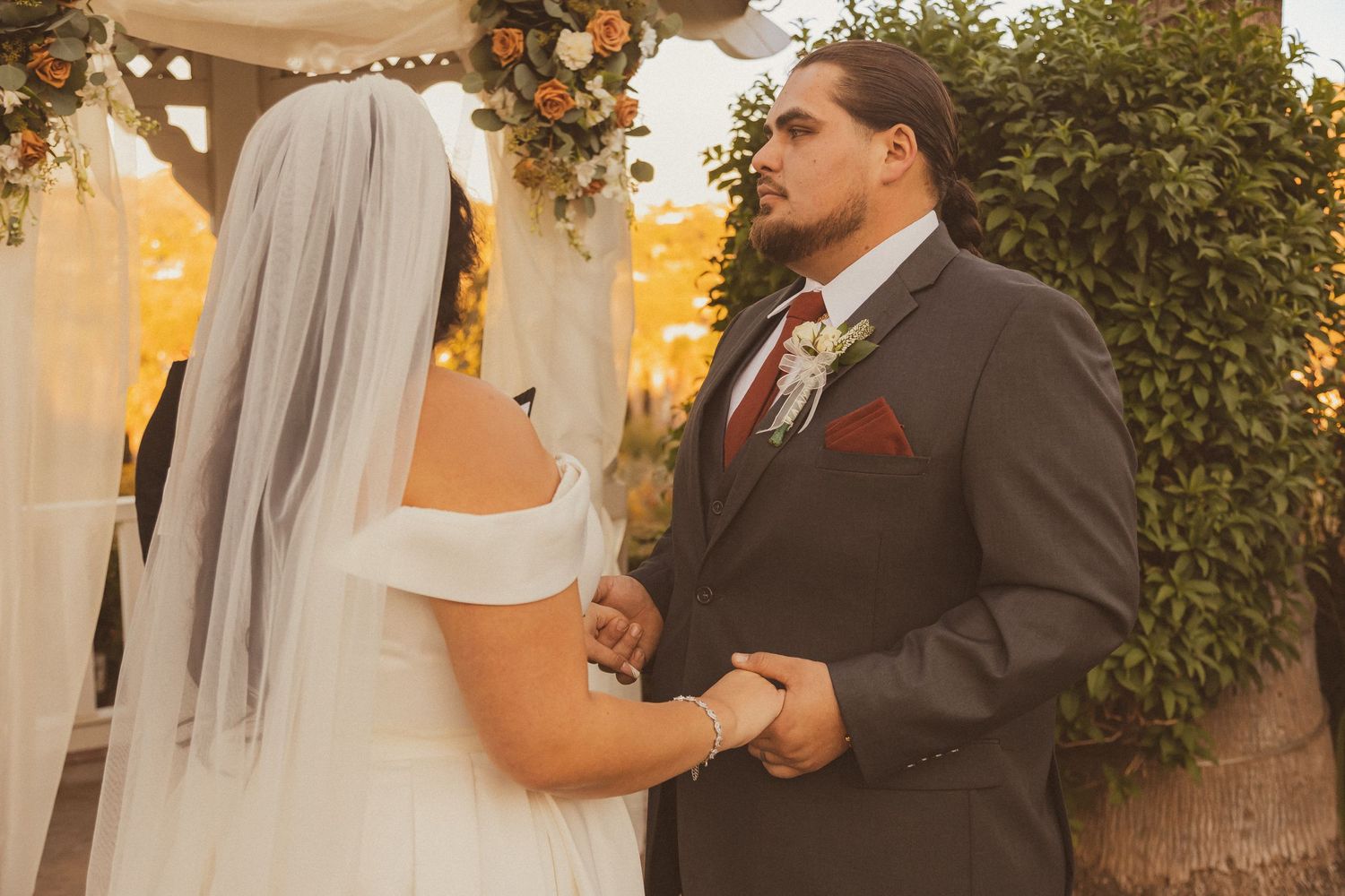 Intimate moment during wedding vows exchange under decorated gazebo at sunset.