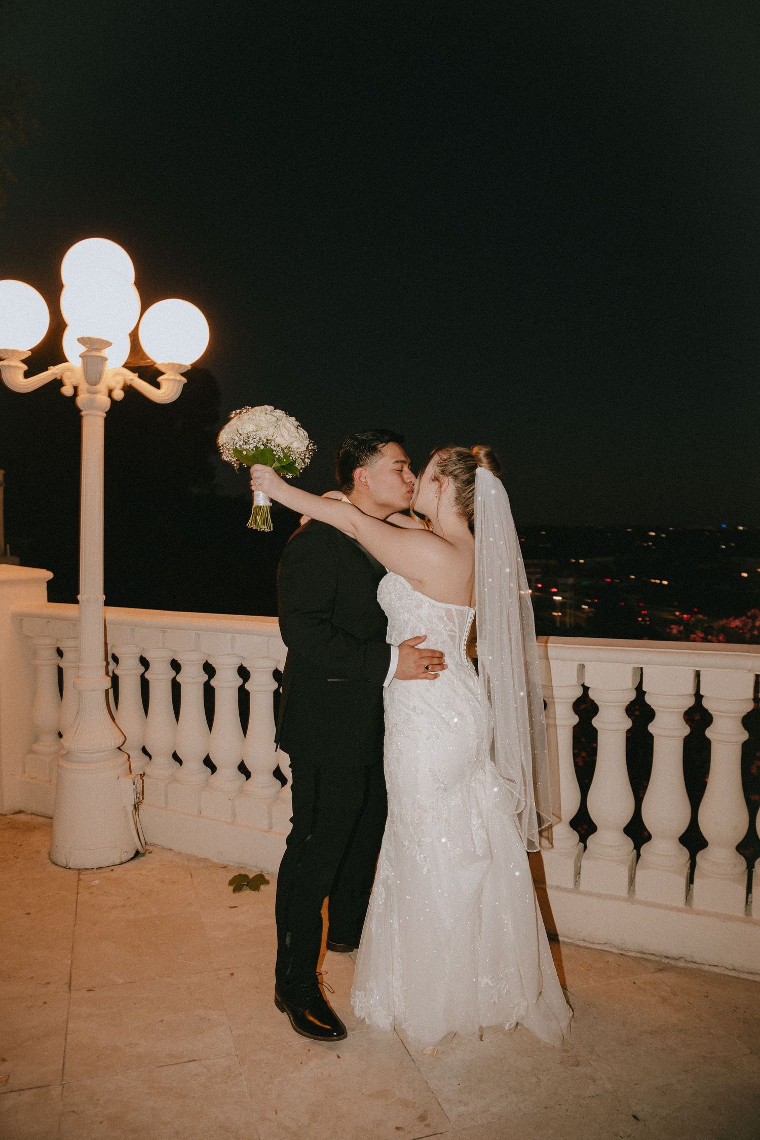 Newlyweds share a romantic dance moment on a beautifully lit terrace at night.