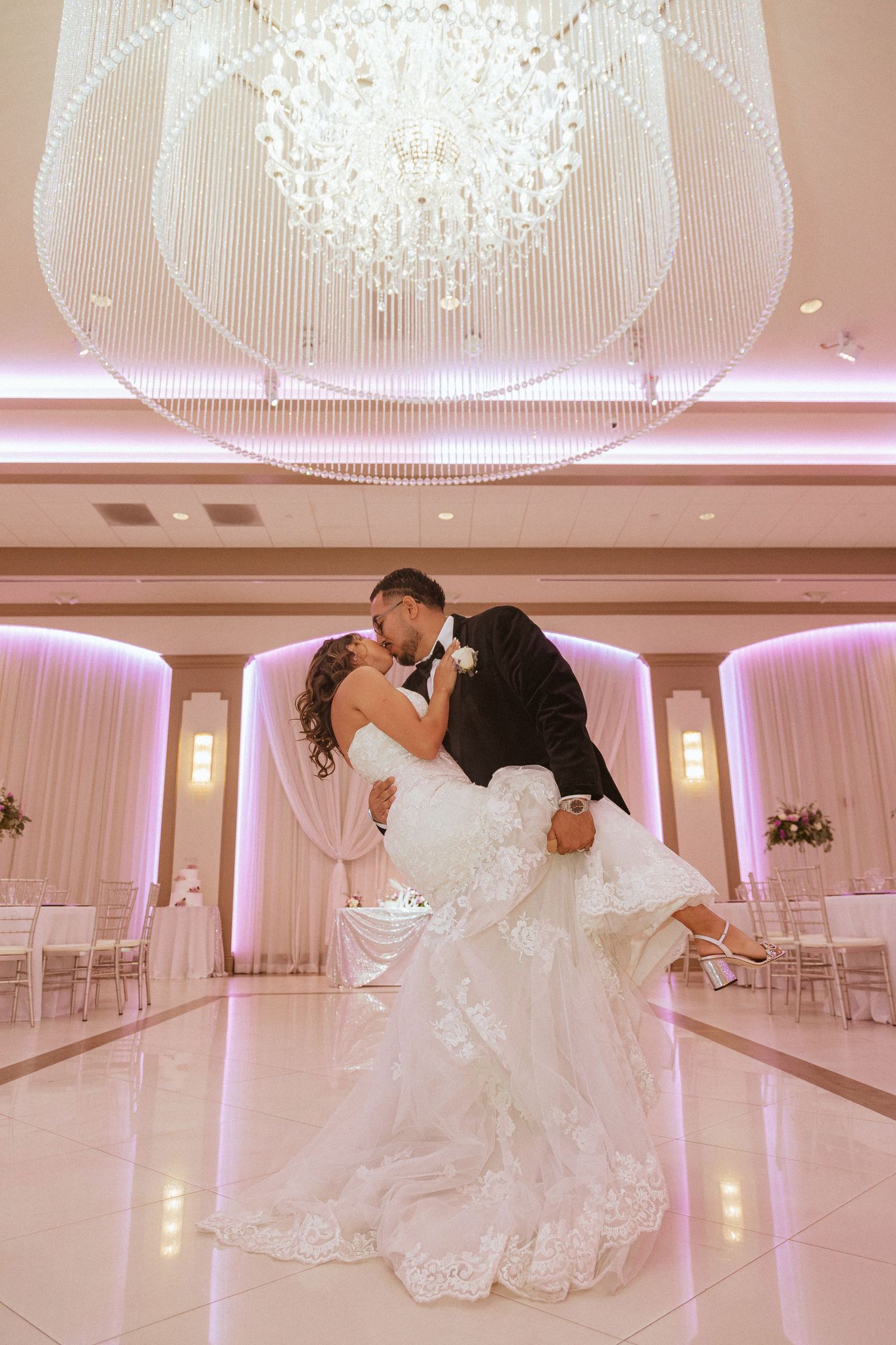 Newlyweds share an intimate ballroom dance moment with a dramatic dip under luxurious lighting.