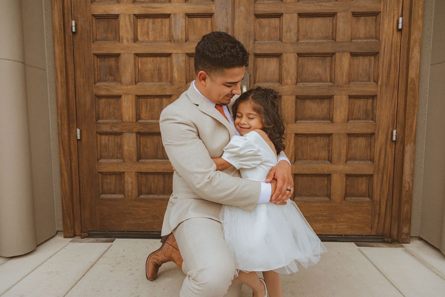 Sweet embrace captured between wedding party members against wooden church door backdrop.