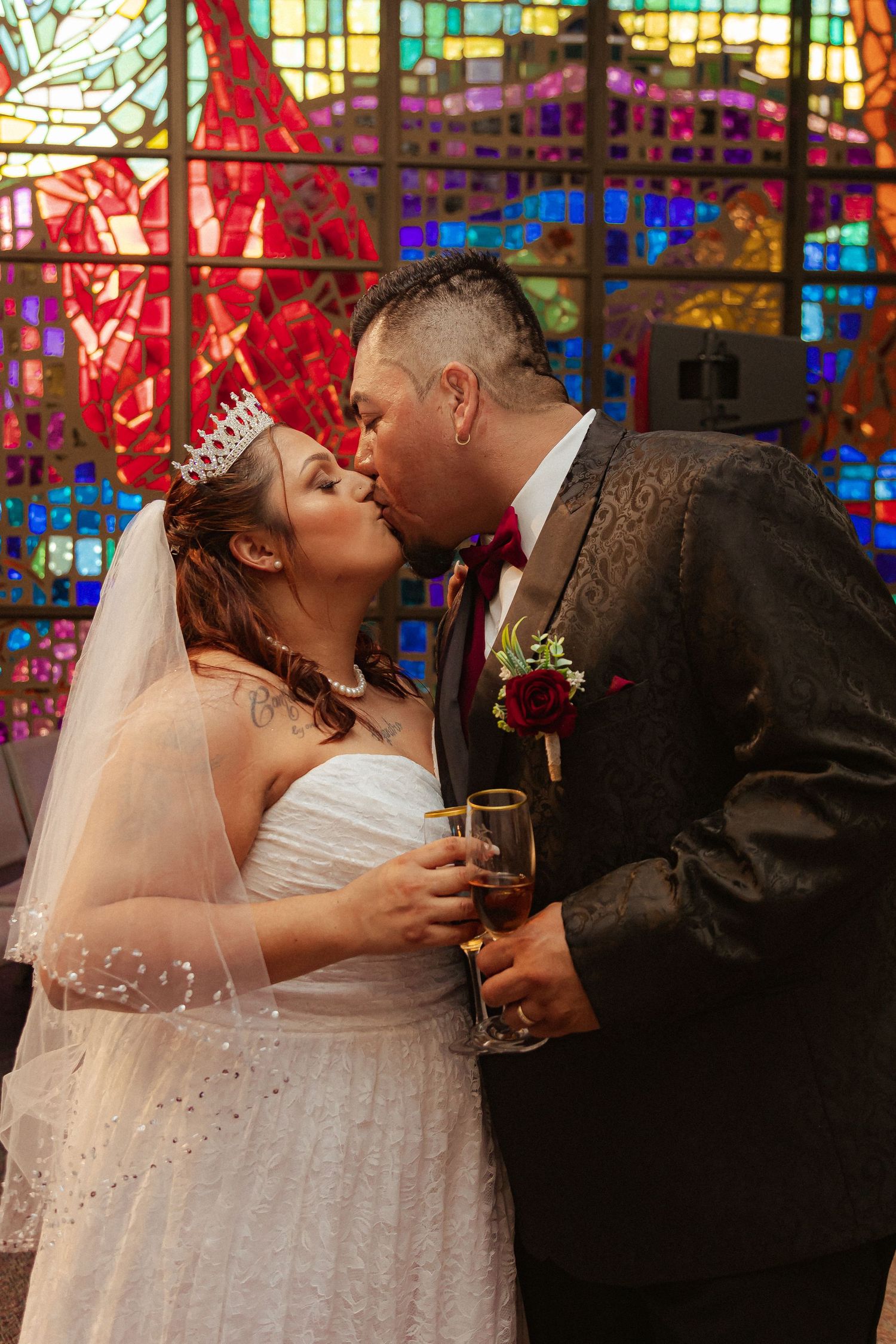 A romantic wedding moment captured in front of colorful stained glass church windows.