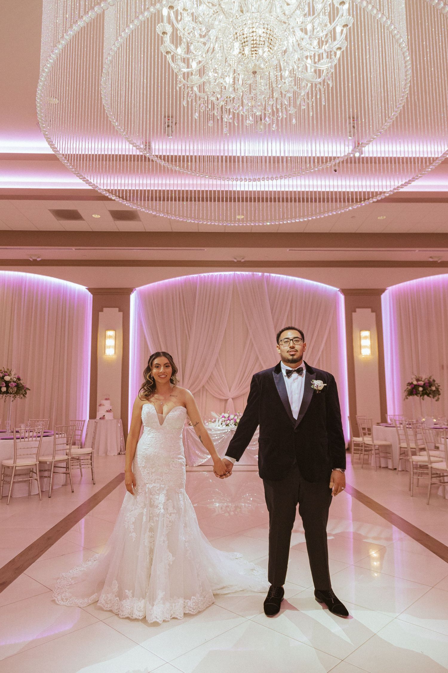 Elegant wedding portrait in a luxurious ballroom with dramatic crystal lighting and pink accents.
