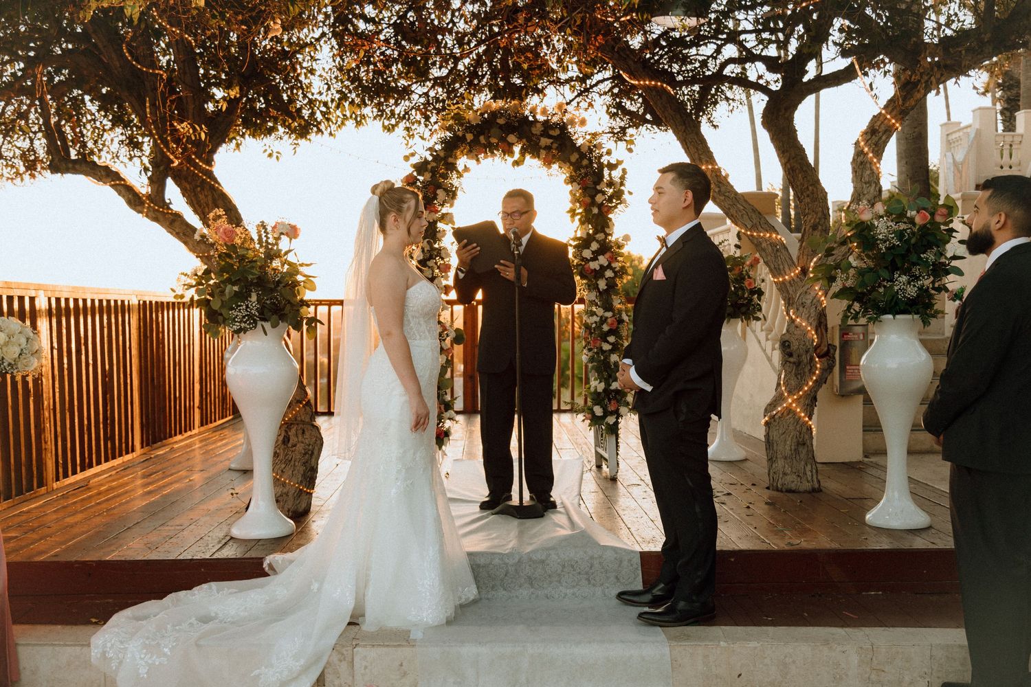 Intimate outdoor wedding ceremony under rustic tree branches with white floral arrangements.