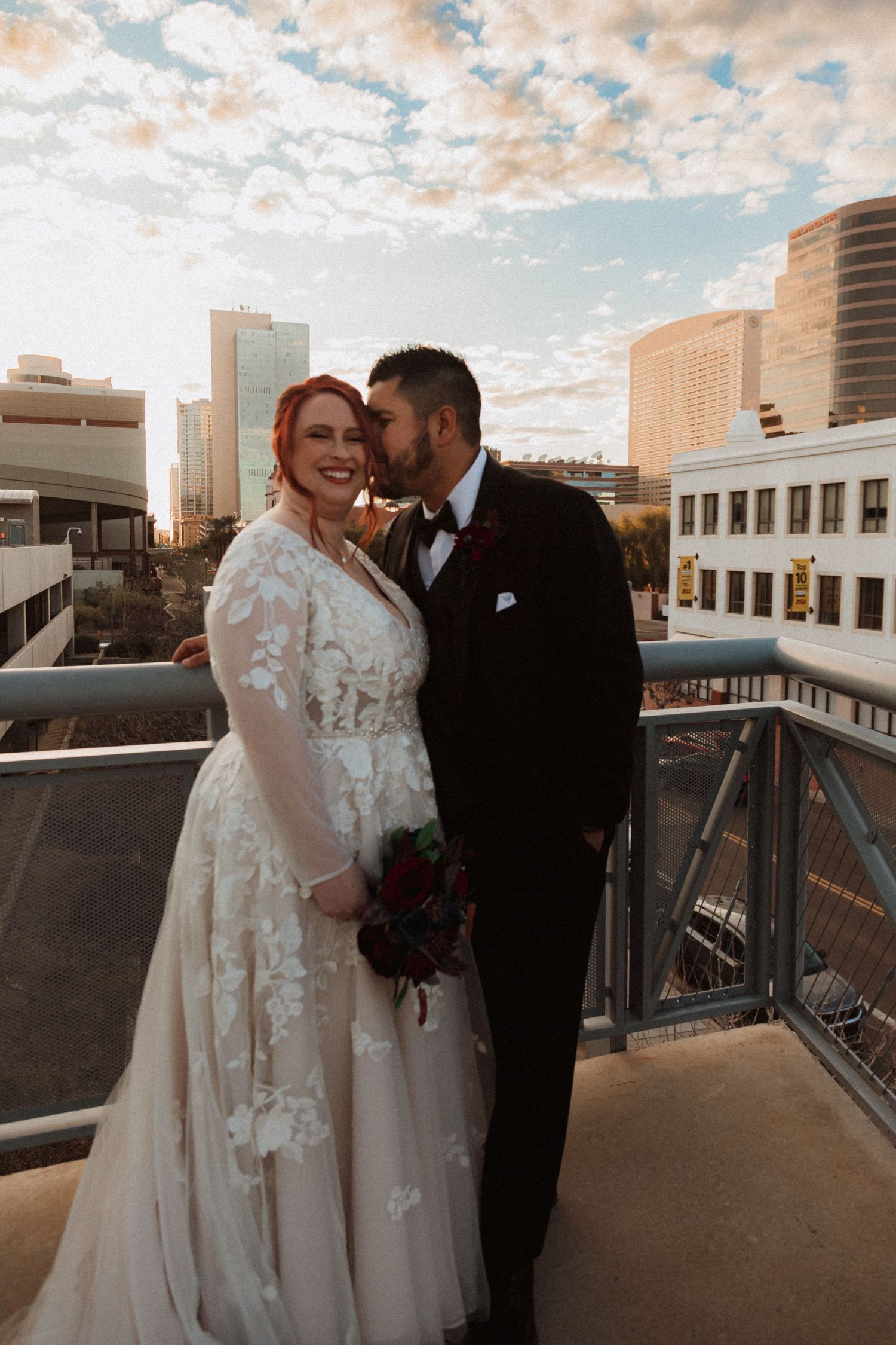 Intimate wedding portrait on city rooftop with warm sunset lighting and downtown buildings.