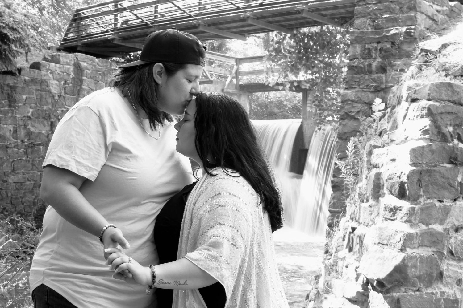 Black and white romantic portrait by a cascading waterfall with stone bridge architecture.