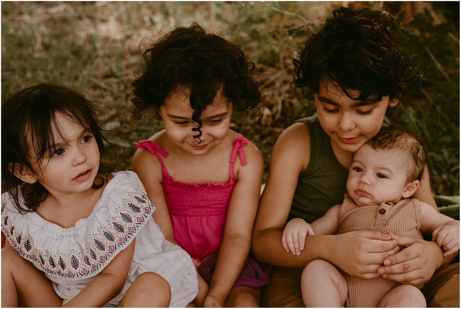 Close-up of children sitting together on a blanket outdoors with warm lighting.