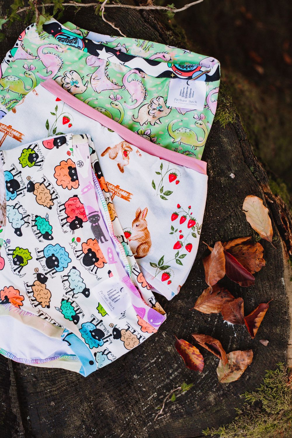 Colorful patterned underwear with cute animal designs displayed on a mossy surface with fallen leaves.