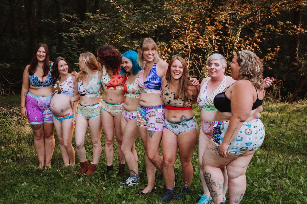 Group wearing colorful patterned swimwear poses together outdoors in a natural setting.