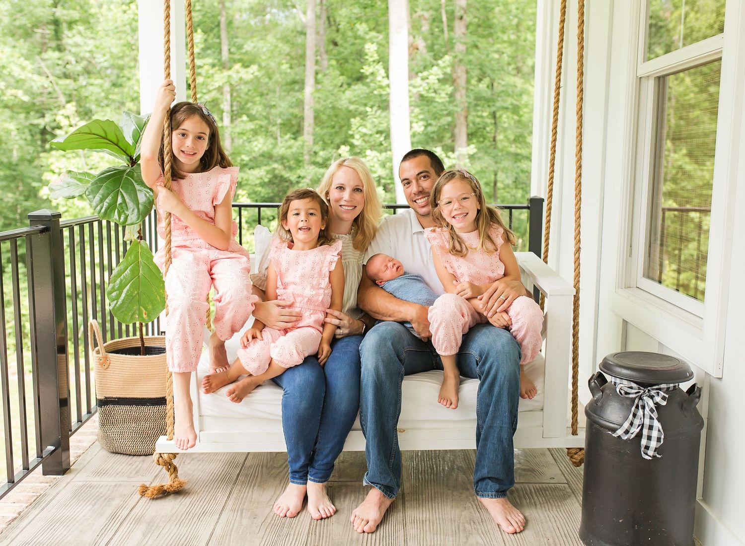Family group relaxing together on a porch swing surrounded by lush green forest views.