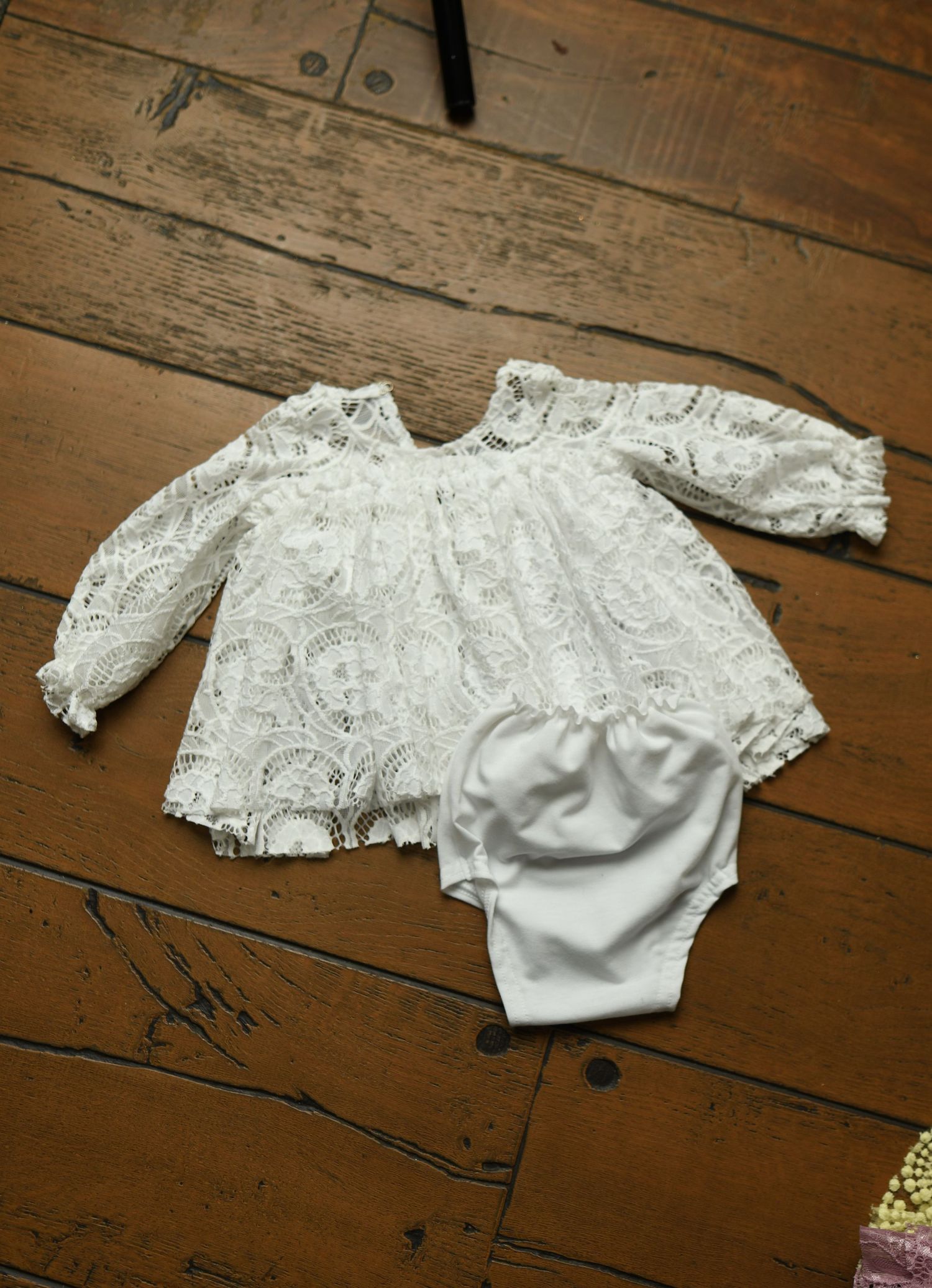 White lace baby romper with satin bloomers displayed on wooden surface.