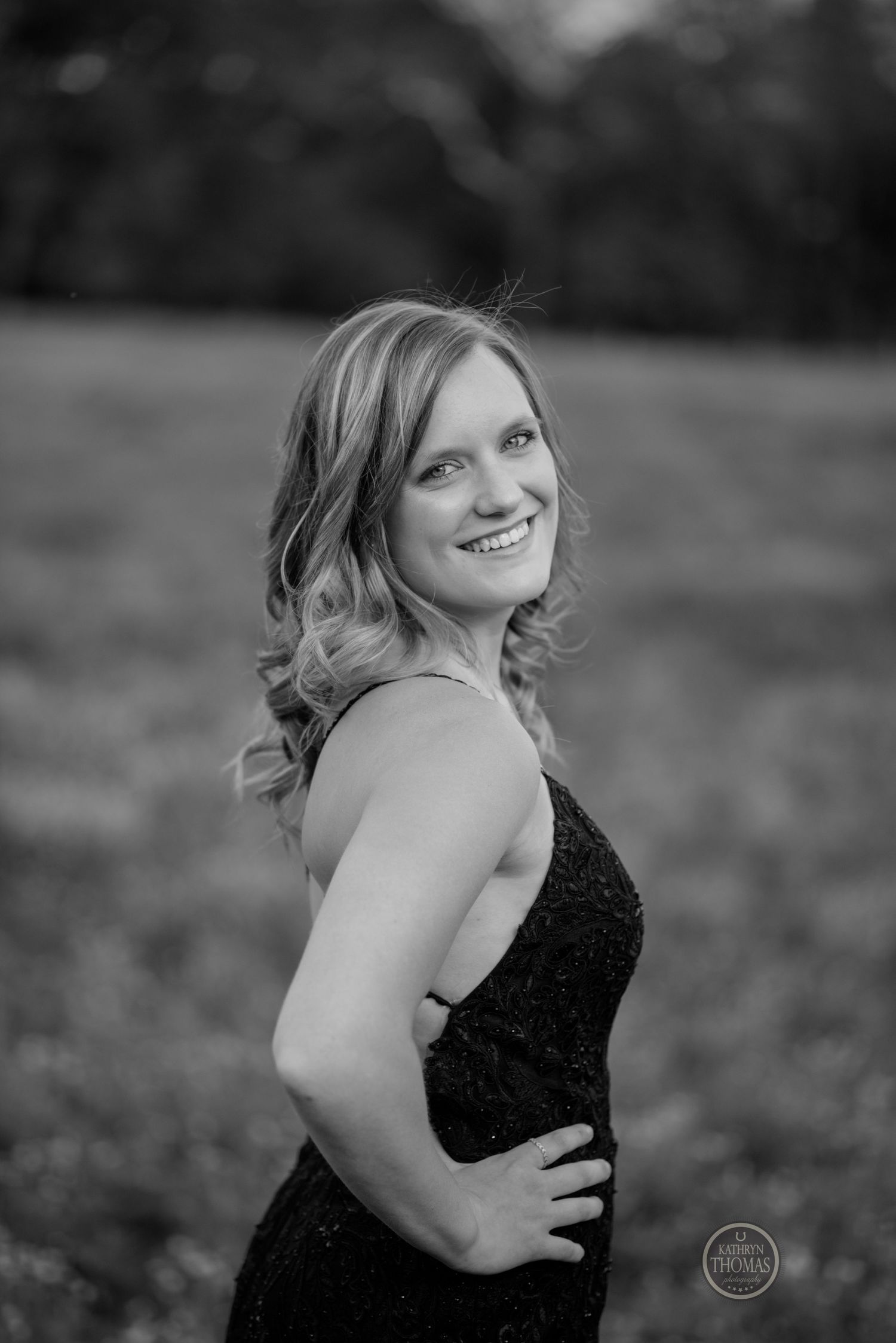 Black and white portrait of woman in formal dress smiling over her shoulder outdoors.