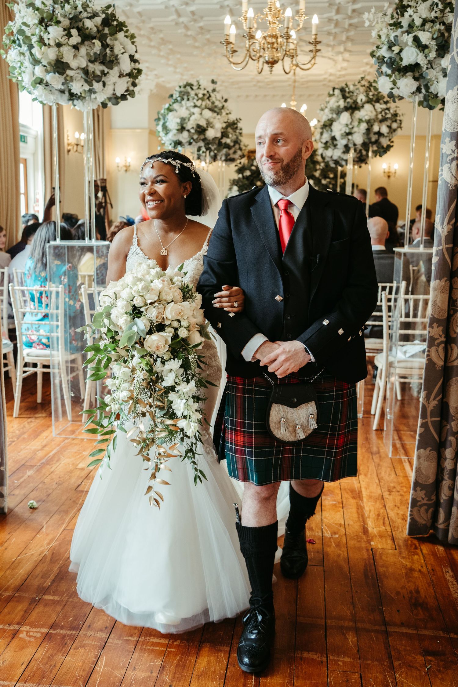 Wedding celebration in elegant ballroom with floral decorations and chandeliers.