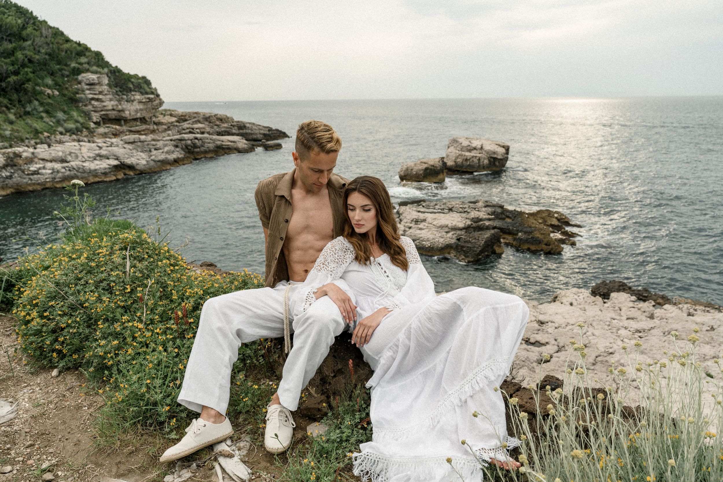 Couple poses on scenic coastal cliff overlooking Mediterranean waters.
